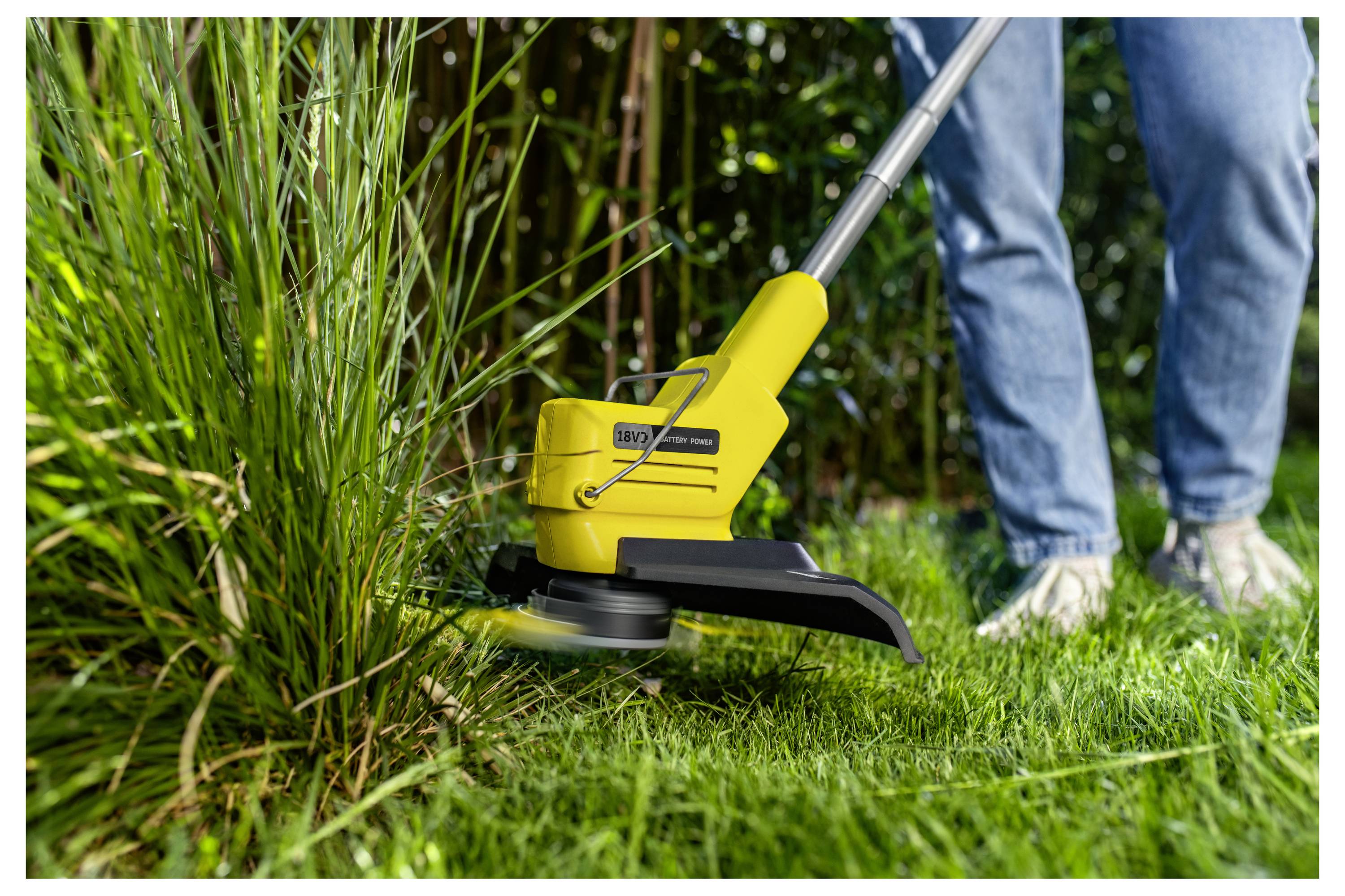 Person mit einem gelben Fadentrimmer, der hohes Gras entlang einer Gartenkante schneidet.