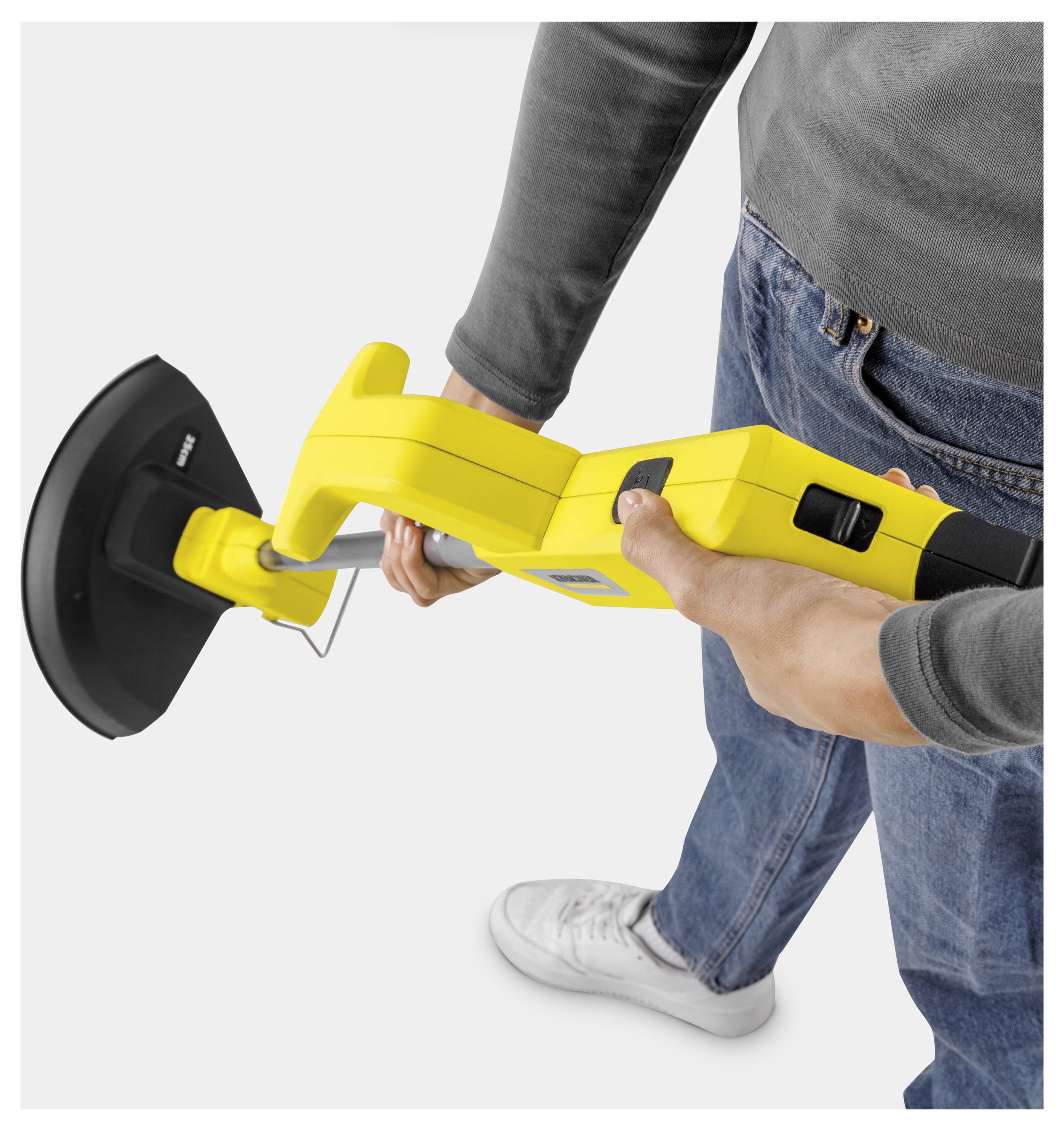 Person hält eine gelbe tragbare Bodenseinimaschine mit einem schwarzen Bürstenkopf, gezeigt bei Verwendung vor einem einfachen weißen Hintergrund.