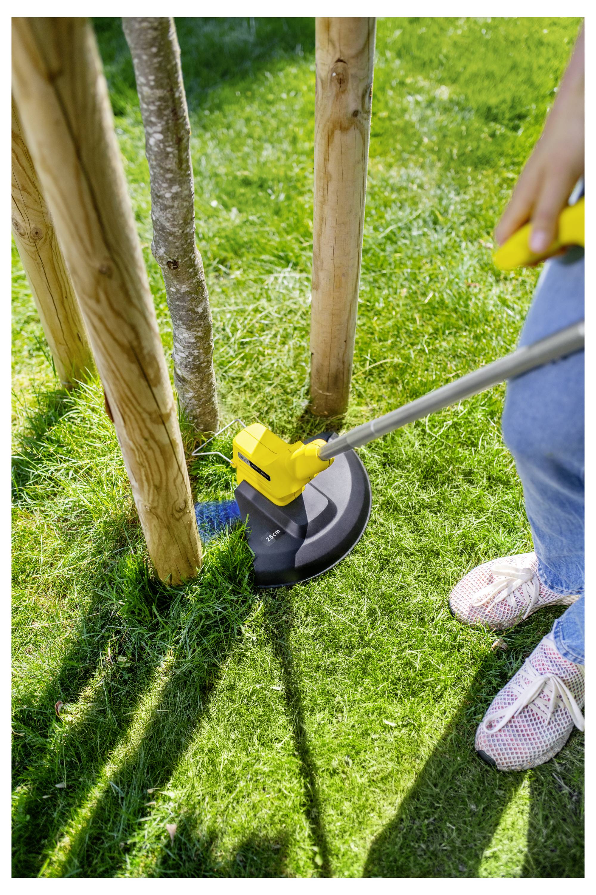 Person, die einen gelben Fadenschneider benutzt, um Gras um Holzpfosten in einem sonnigen Garten zu schneiden