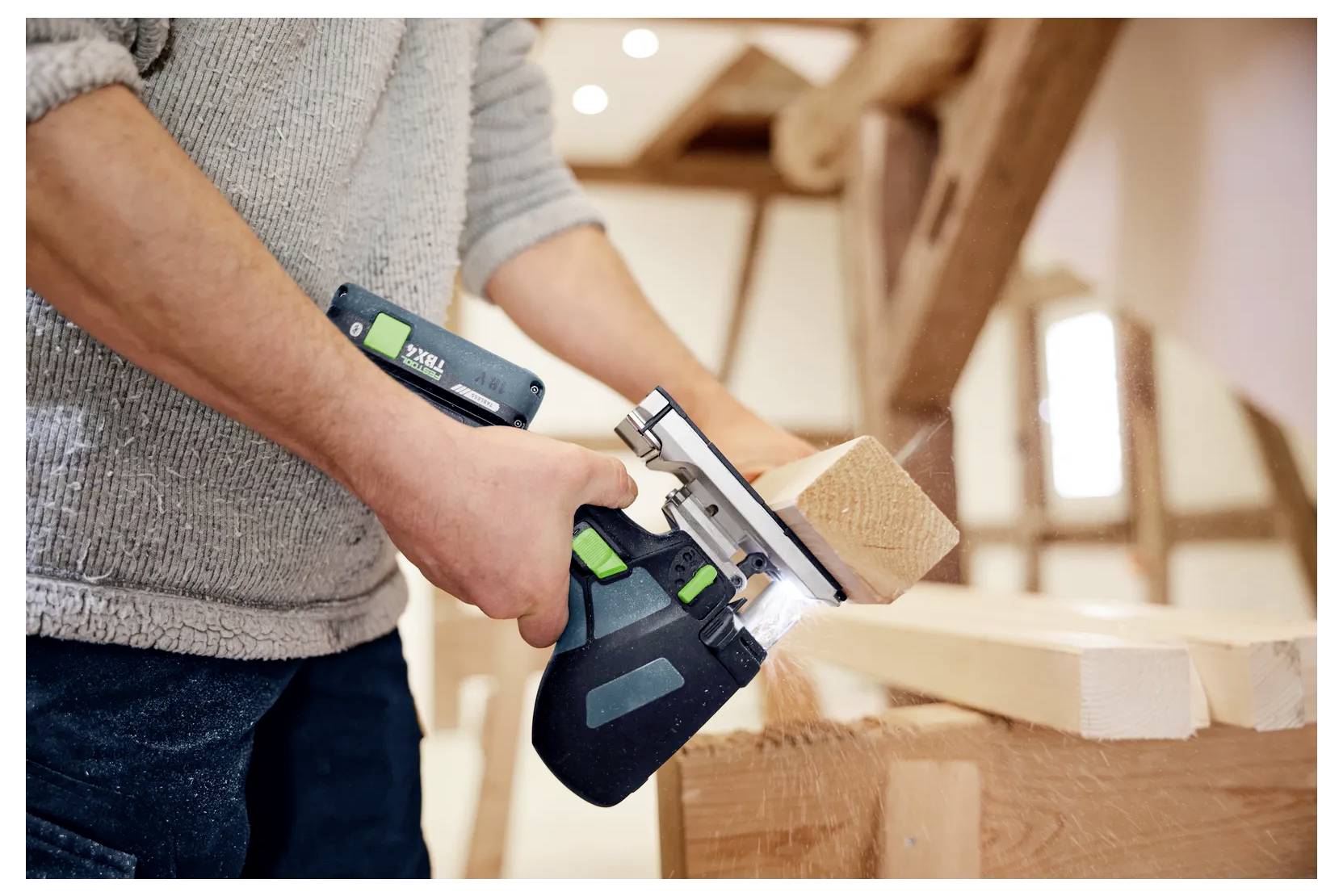 Person, die einen tragbaren Elektrobobel verwendet, um eine Holzplanke in einer Werkstatt zu hobeln, wobei Holzspäne auf die Werkbank fallen.