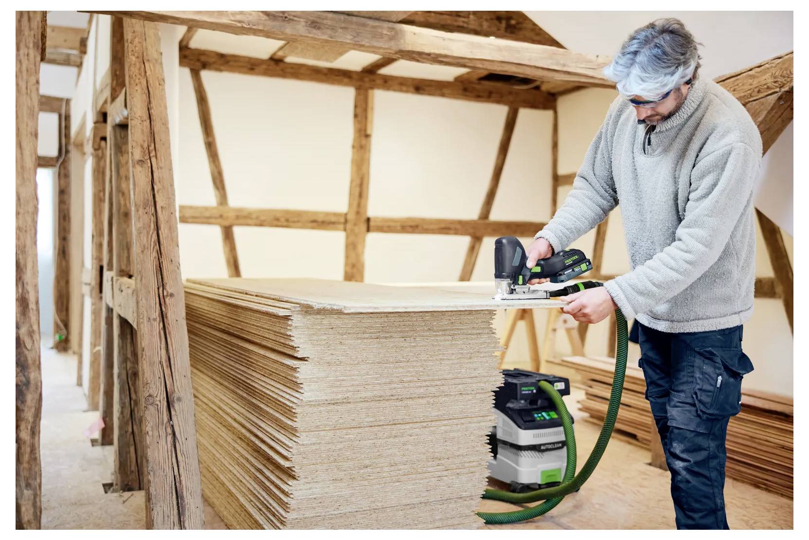 Ein Arbeiter, der einen tragbaren Elektroschleiffer auf einem Stapel von Holzbrettern in einer Holzwerkstatt verwendet.