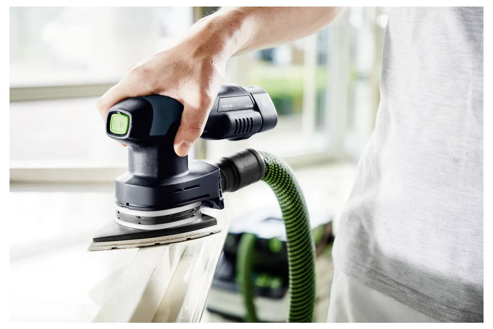 Hand verwendet einen tragbaren Elektroschleiffer mit Staubschlauch zum Glätten einer Holzoberfläche in Innenräumen.