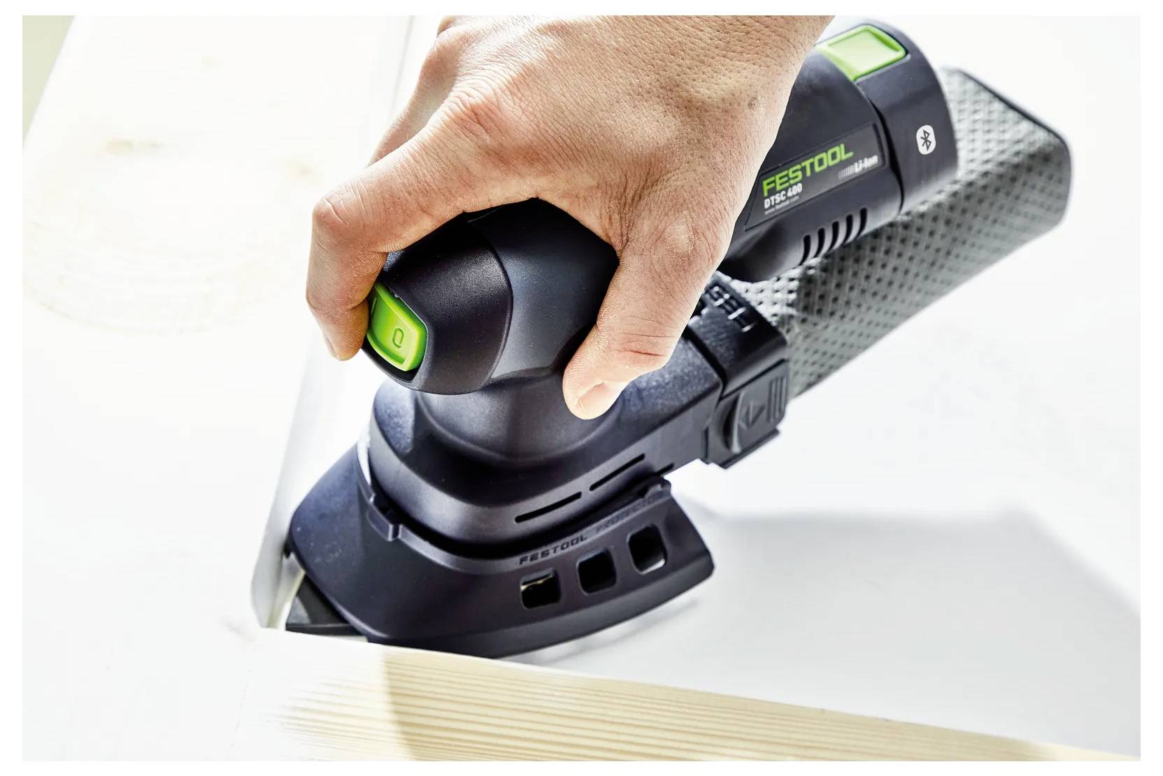 Hand, die einen Festool-Elektroschleiffer auf einer weißen Oberfläche verwendet, glättet die Kante eines Holzbretts.