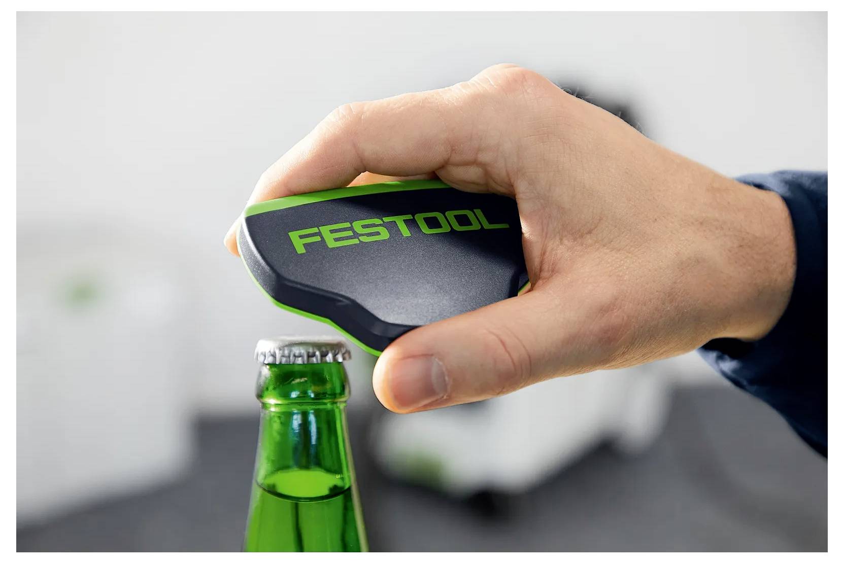 Hand, die einen FESTOOL-Flaschenöffner verwendet, um einen grünen Glaschraubverschluss aufzuhebeln.