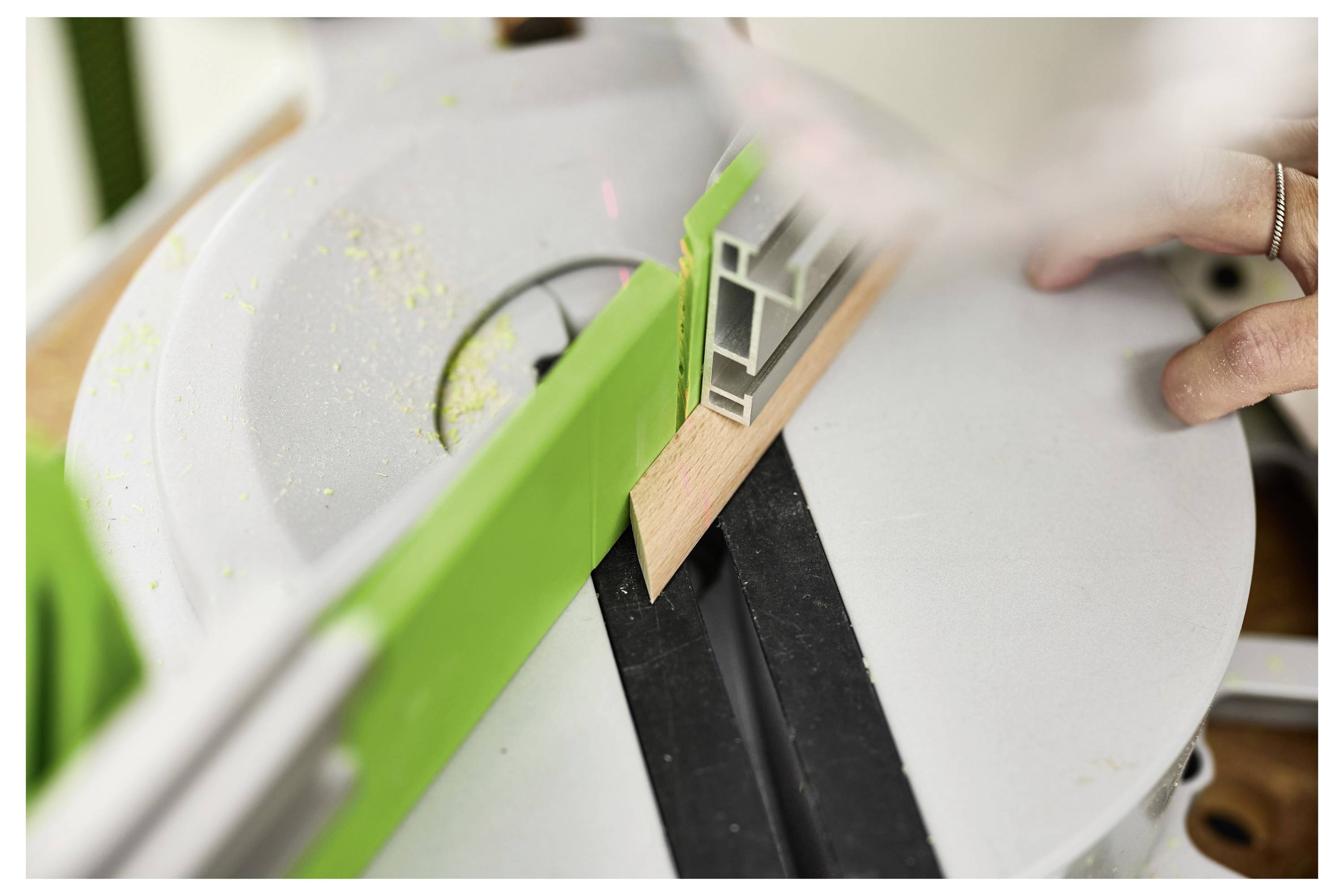 Nahaufnahme einer Gehrungssäge, die ein graues PVC-Zierleistenstück schneidet, während eine Hand das Material auf dem Sägetisch stabilisiert.