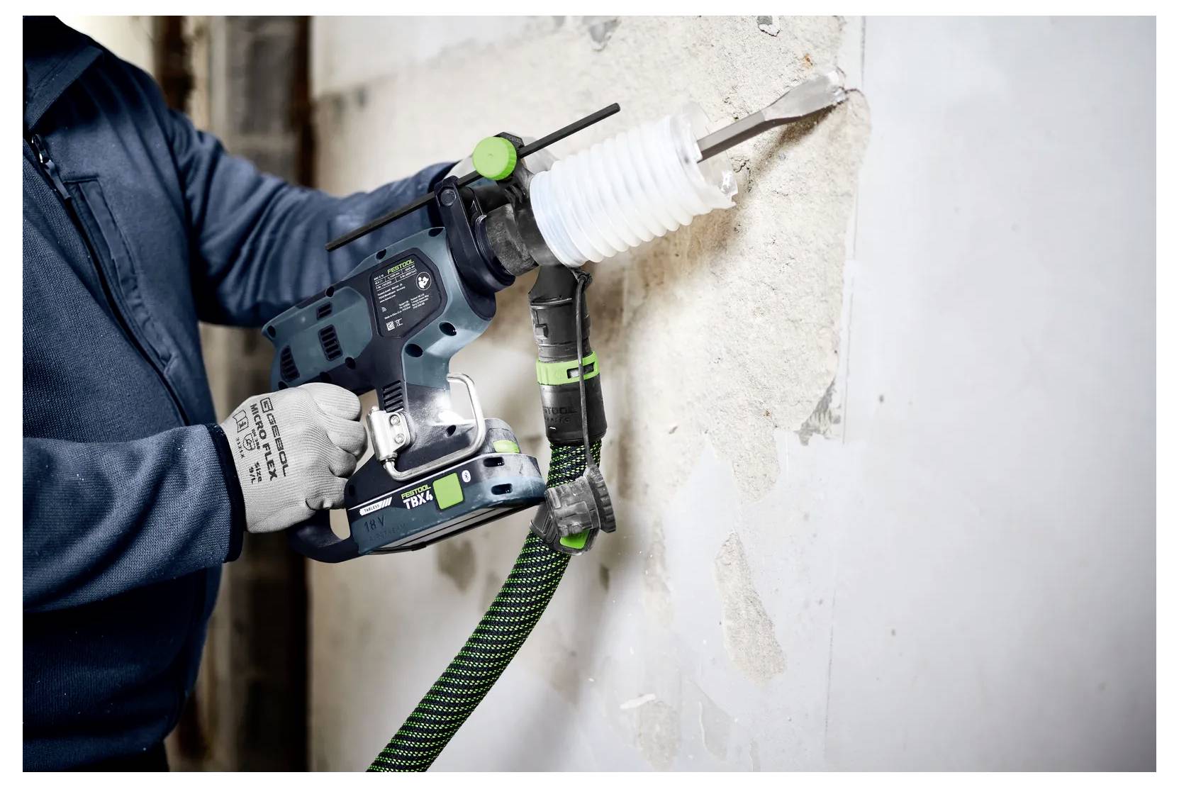 Arbeiter, der mit einer Elektrobohrmaschine mit Staubabsaugung ein Loch durch eine Wand bohrt, während einer Bau- oder Reparaturarbeit.