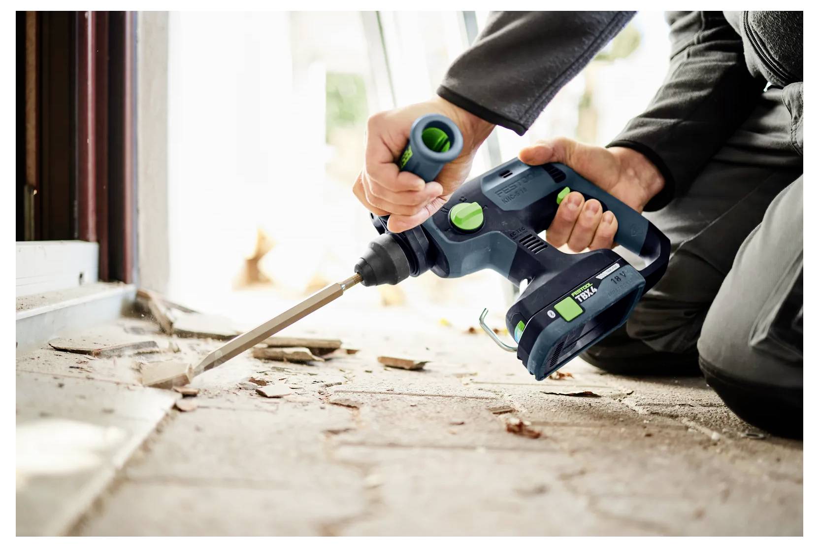 Person mit einem kabellosen Abbruchhammer, der während einer Renovierung einen Boden oder eine Wand aufbricht.