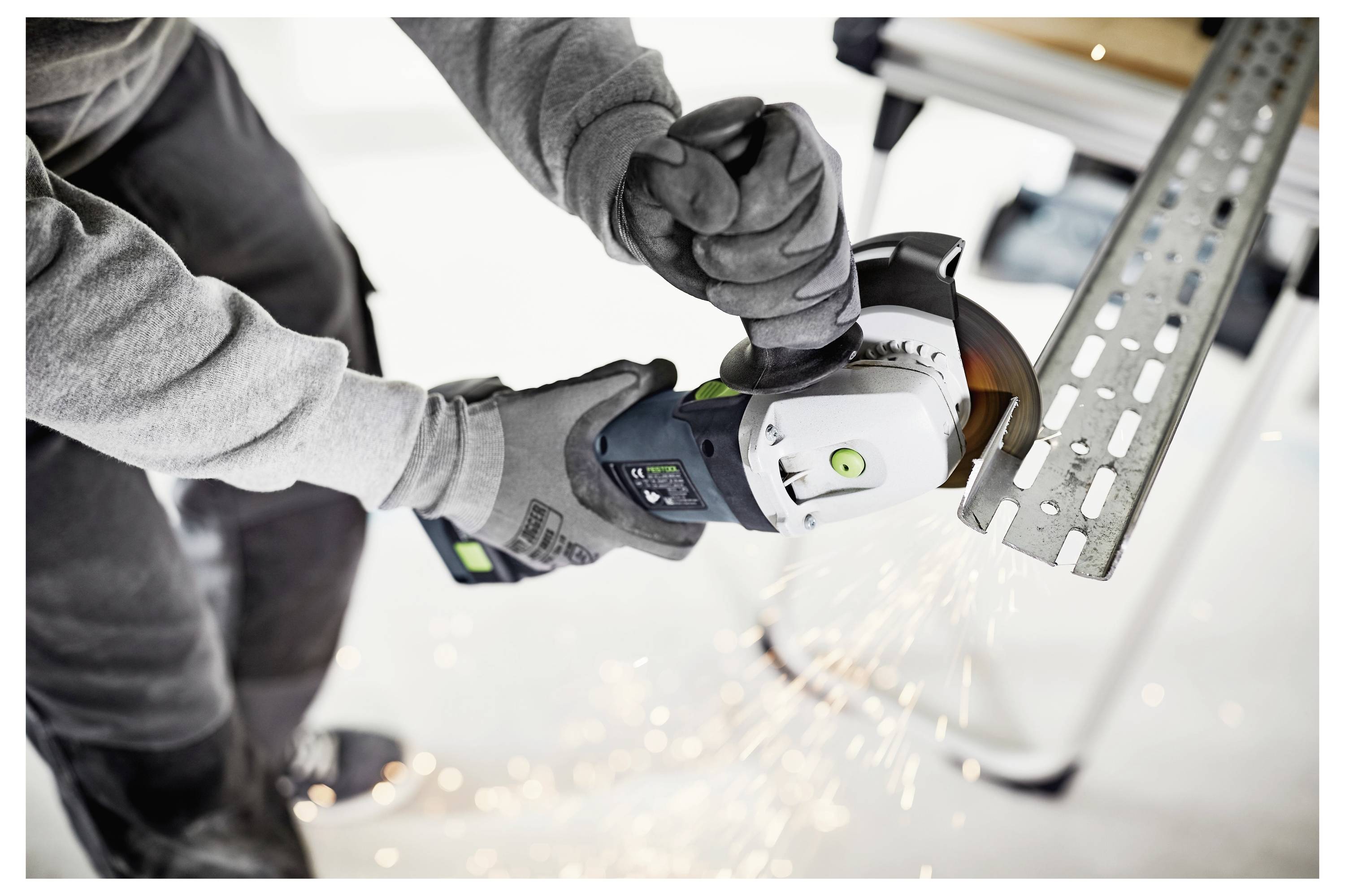 Person mit einem Winkelschleiffer, der auf einem Stahlträger arbeitet und dabei Funken erzeugt, während er Stahl in Innenräumen schneidet oder schleift.