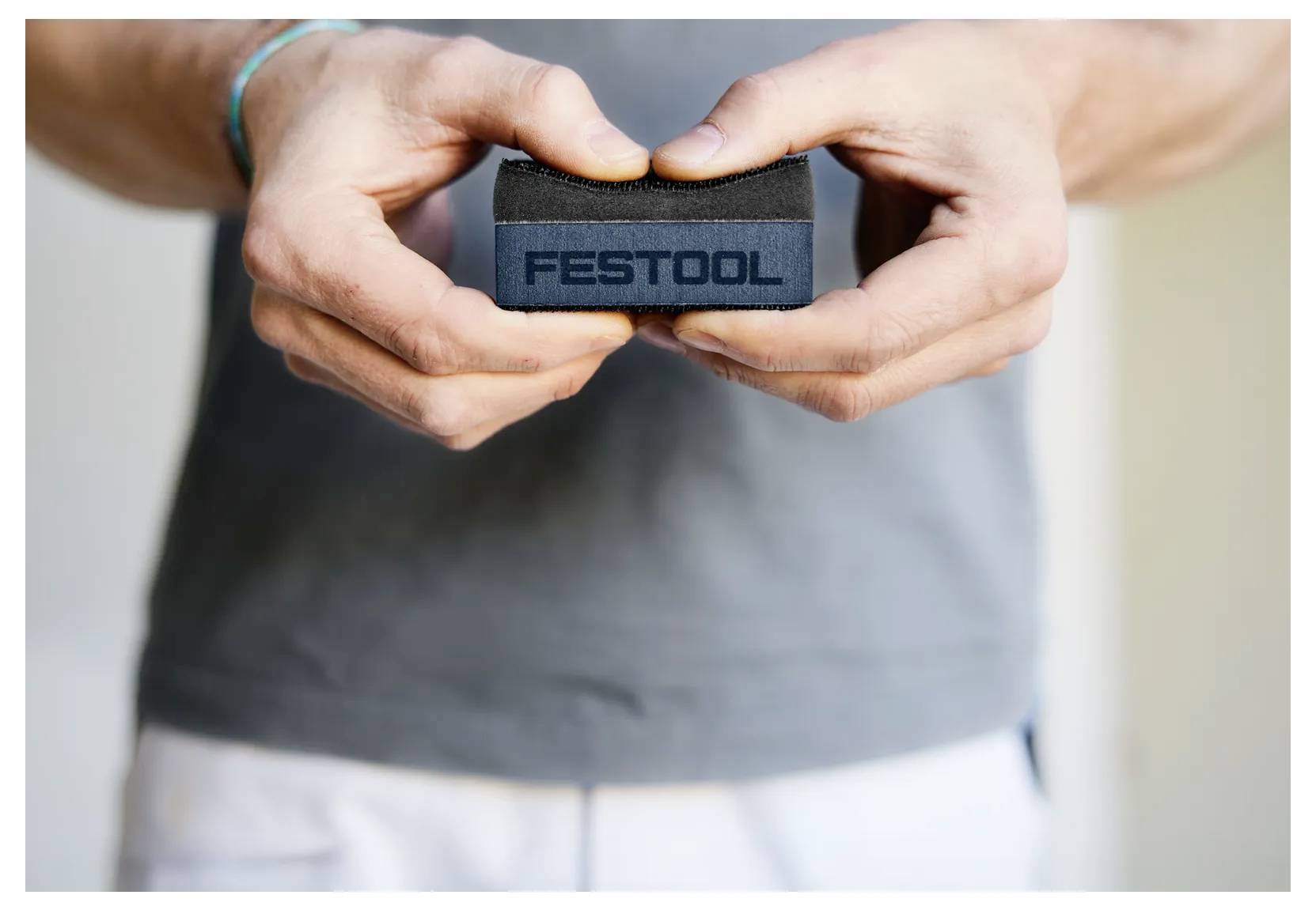 Hände halten einen kleinen schwarzen Stoffriemen mit der Aufschrift „FESTOOL