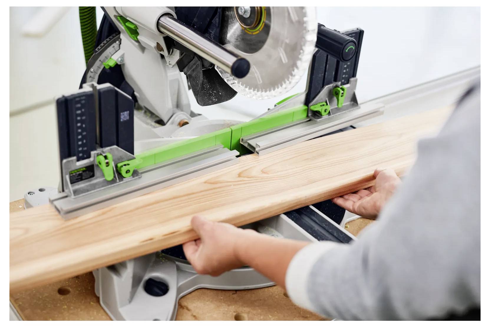 Person, die eine Kappsäge verwendet, um ein Holzbrett zu schneiden, wobei Sicherheitsklammern das Holz an Ort und Stelle halten.