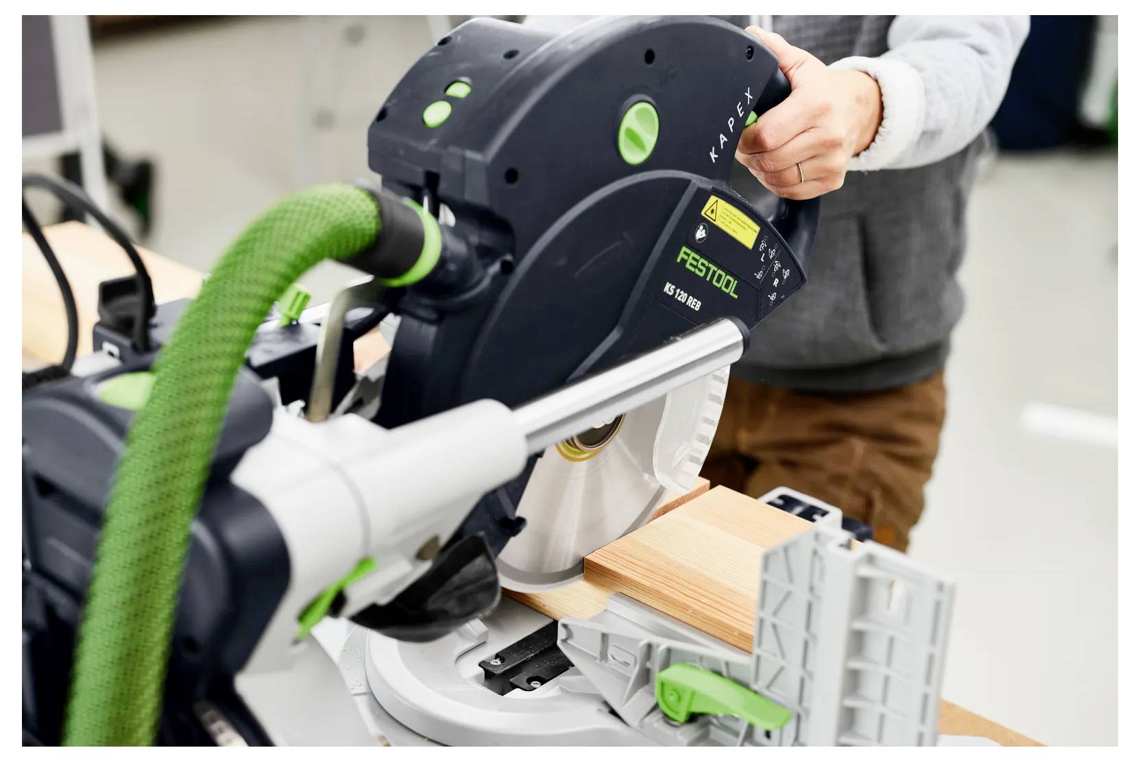 Eine Person, die eine Festool-Gehrungssäge bedient, um ein Holzbrett in einer Werkstatt zu schneiden.