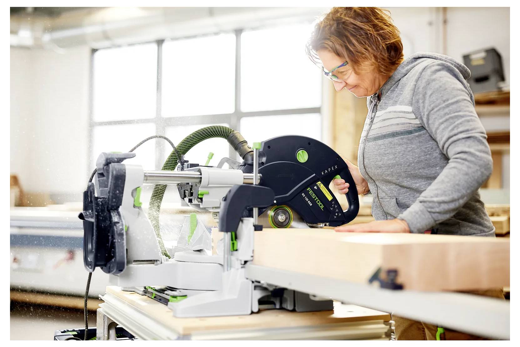 Frau, die eine Elektrosäge verwendet, um ein langes Holzbrett in einer Werkstatt zu schneiden, konzentriert auf die Schneidaufgabe.