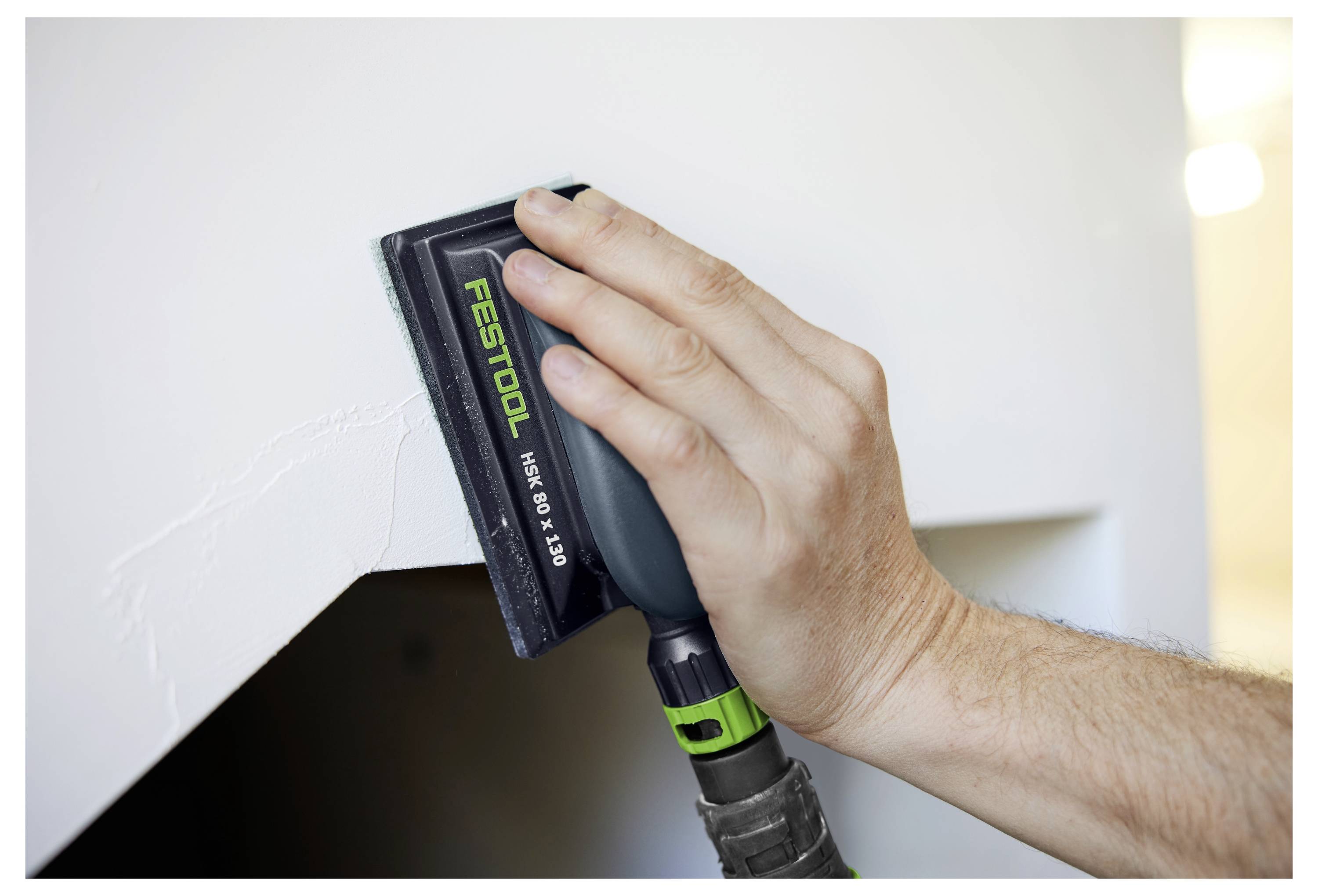 Mit einem Festool-Schleiffer die Ecke einer weißen Wand von Hand abschleifen, um die Oberfläche vor der Fertigstellung zu glätten.