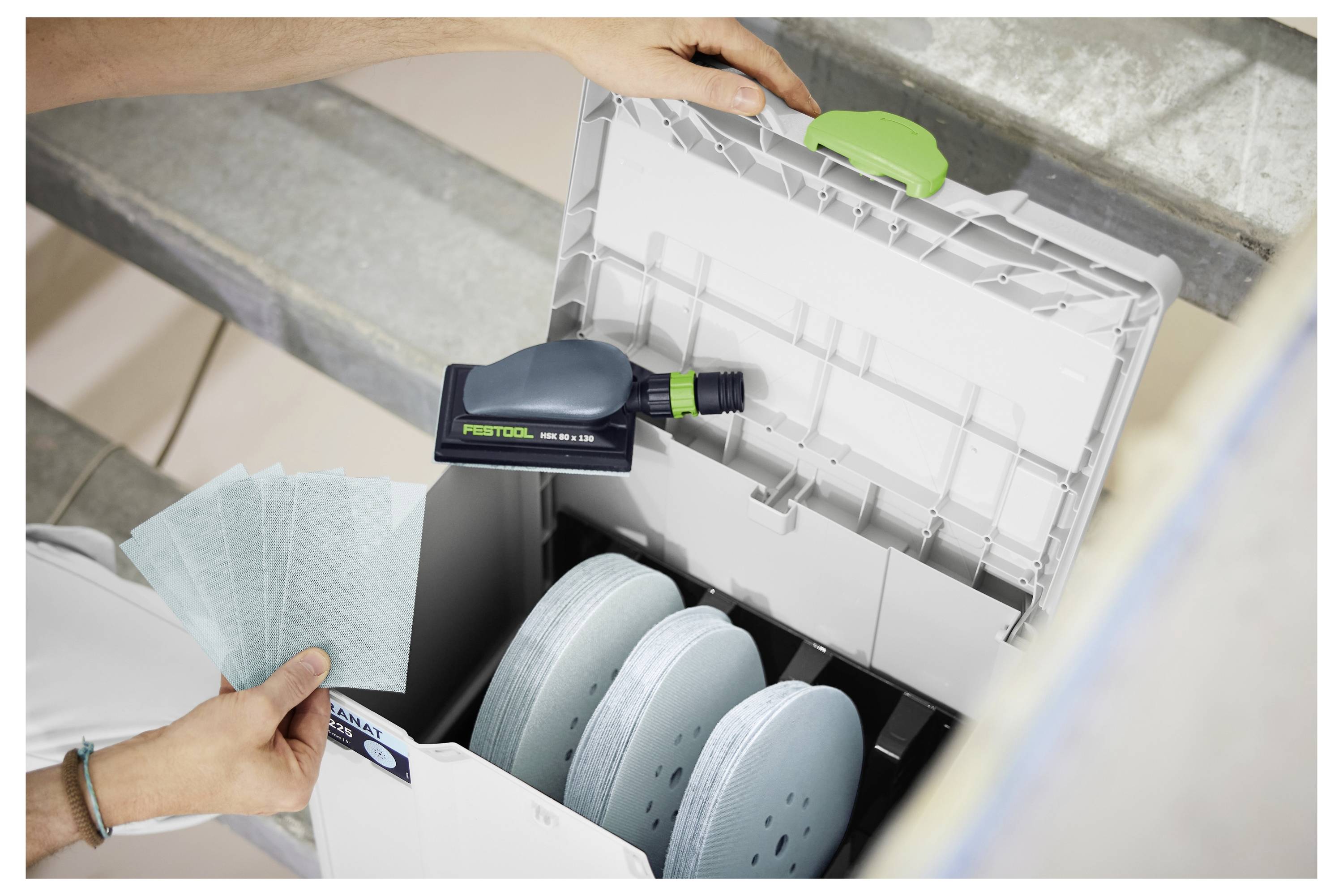 Hände, die Schleifteller in eine Festool Systainer-Aufbewahrungsbox mit einem darin befestigten Elektrowerkzeug einlegen.