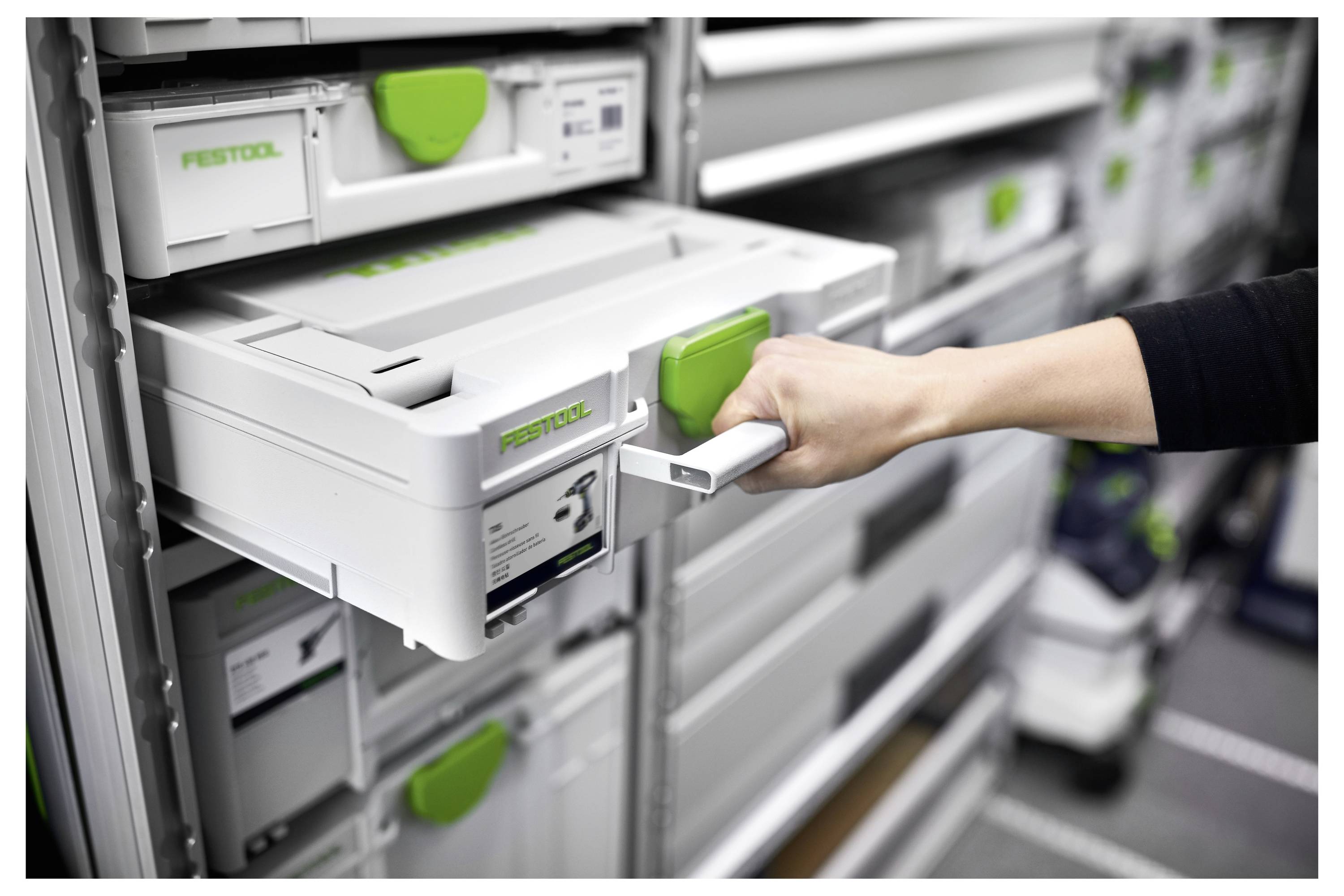 Hand, die eine grün verriegelte Festool-Aufbewahrungsschublade aus einer Wand mit gestapelten Werkzeugorganizern herauszieht.