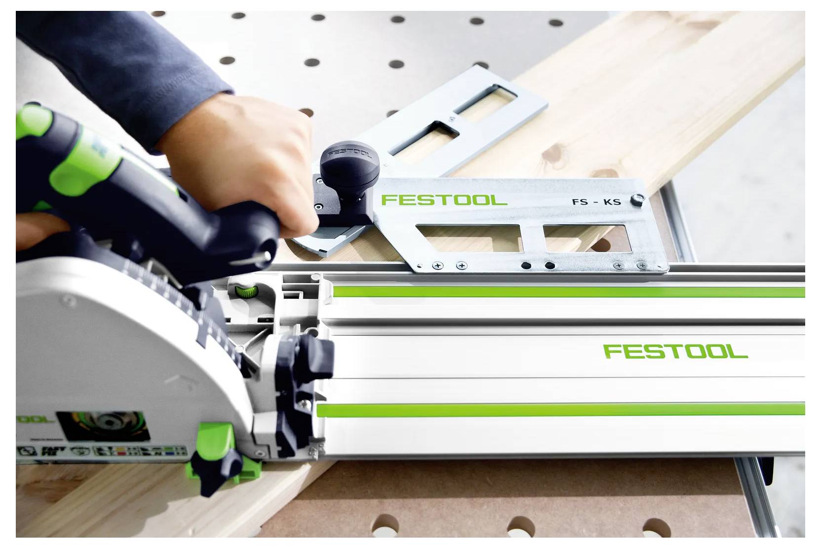Nahaufnahme einer Festool-Kreissäge, die ein Holzbrett entlang einer Führungsschiene schneidet, während eine Hand das Werkzeug sicher hält.