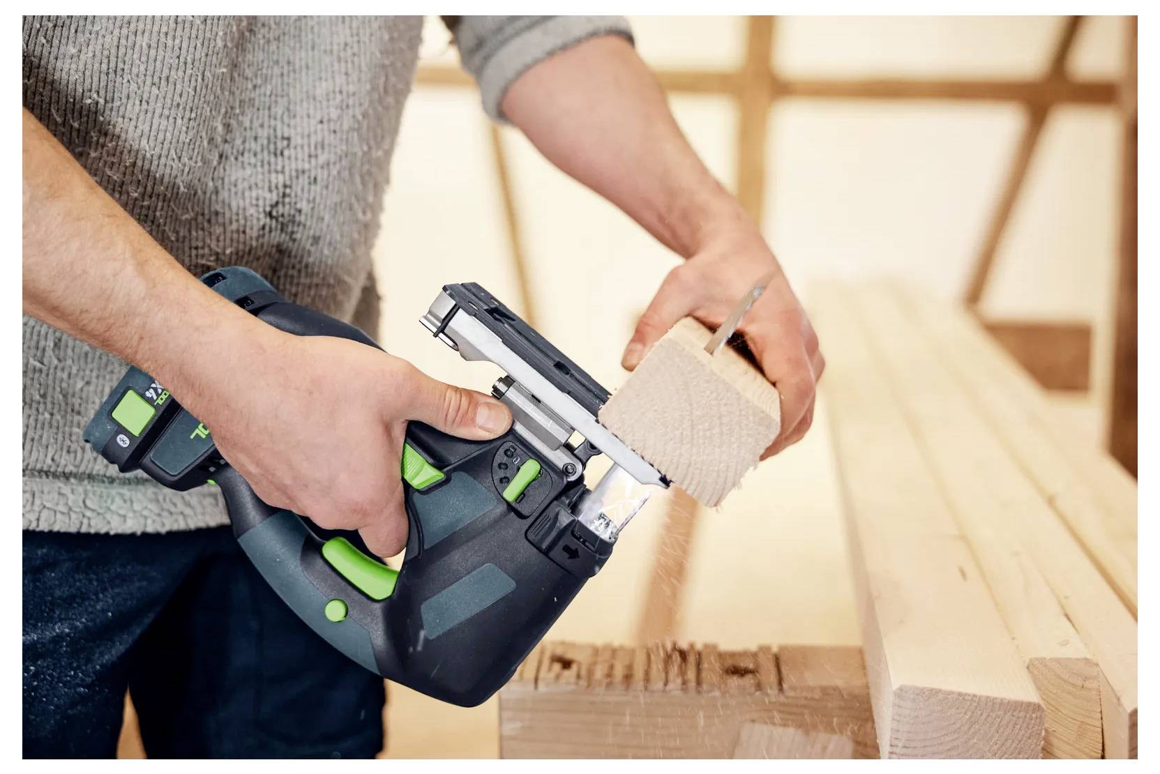 Person, die eine kabellose Elektrosäge benutzt, um ein Holzbrett in einer Werkstatt zu schneiden.
