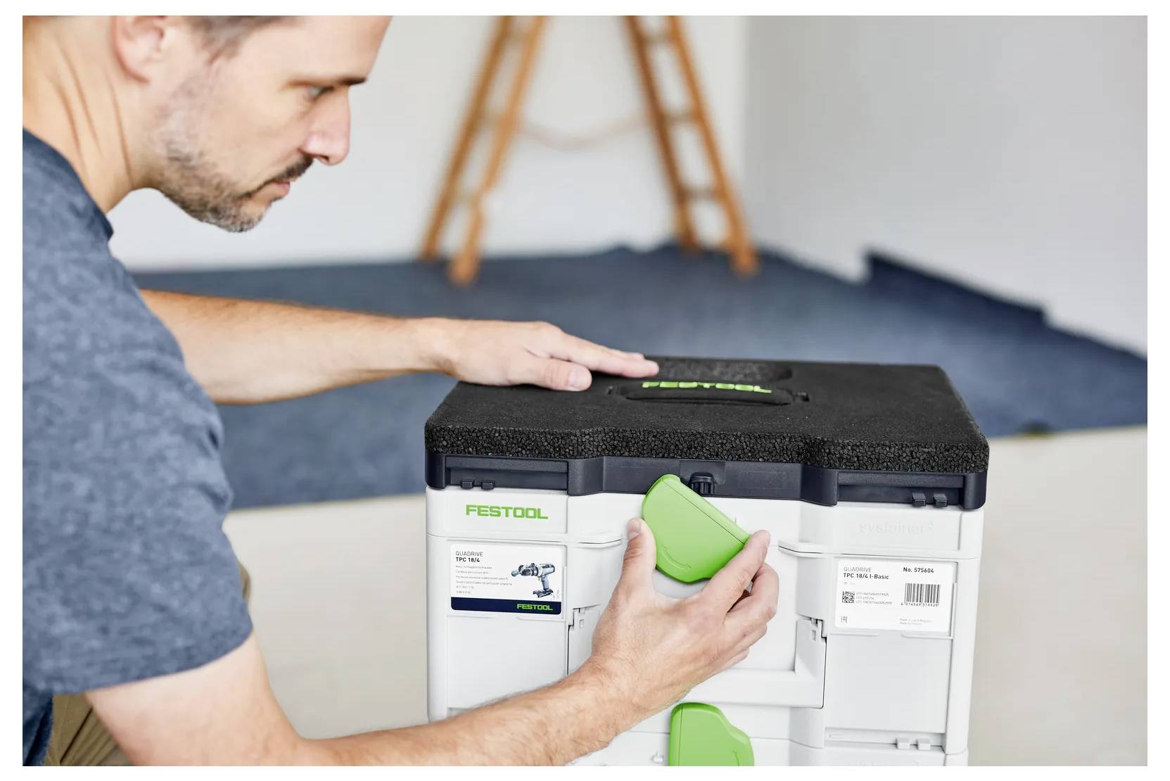 Ein Mann, der einen grünen Riegel verwendet, um einen Festool-Lagerbehälter in einer Werkstatt- oder Heimumgebung zu öffnen.