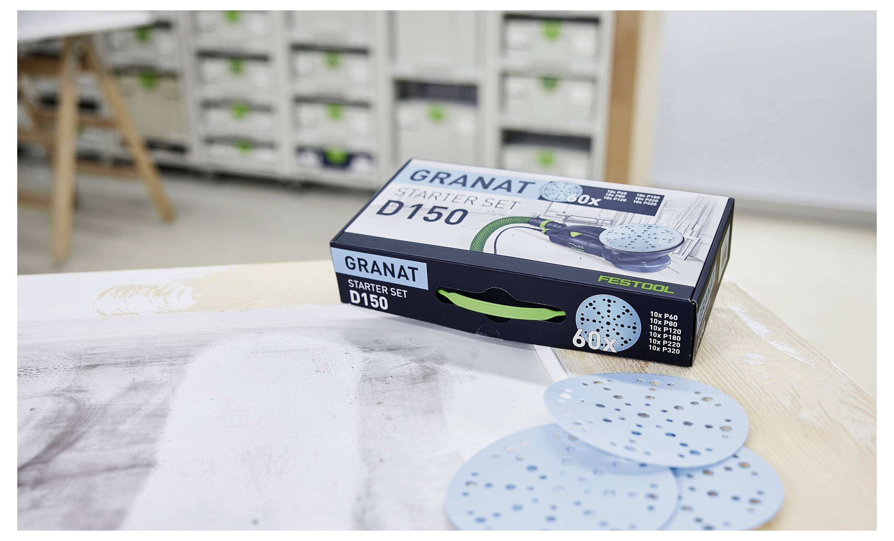 Festool GRANAT Starter Set D150 Schachtel auf einer Werkbank, mit blauen Schleiftellern daneben in einer Werkstatt ausgebreitet.