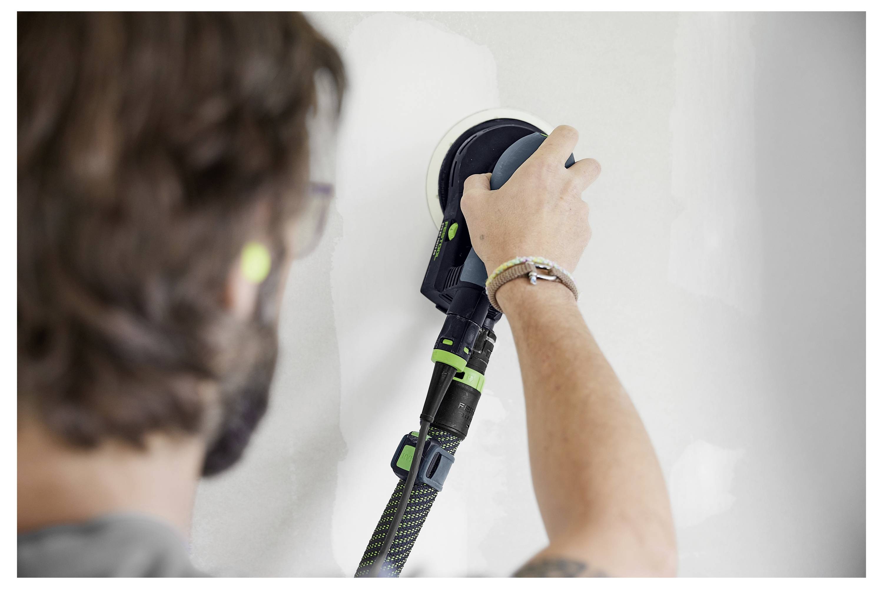 Person, die während einer Wohnungsrenovierung eine Wand mit einem tragbaren Elektroschleiffer abschleifen, um eine weiß gestrichene Oberfläche zu glätten.