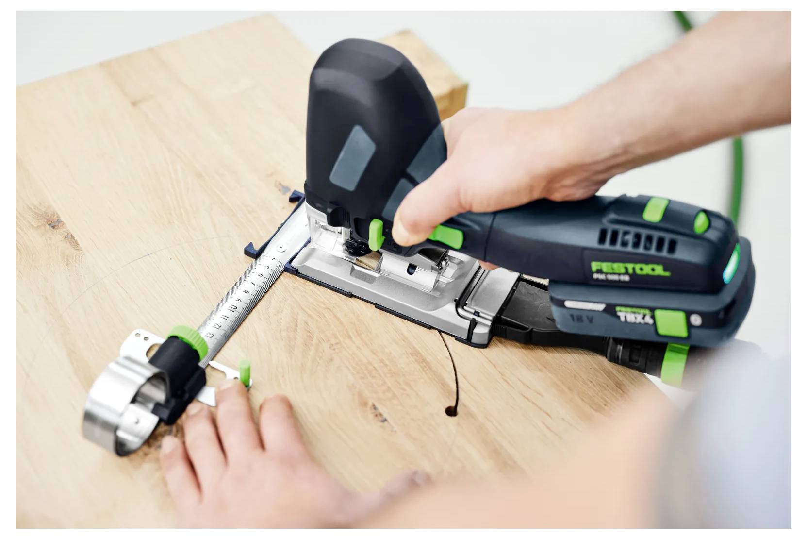 Person using a cordless jigsaw with a guide rail to cut a wooden board.---Person, die eine kabellose Stichsäge mit einer Führungsschiene verwendet, um ein Holzbrett zu schneiden.