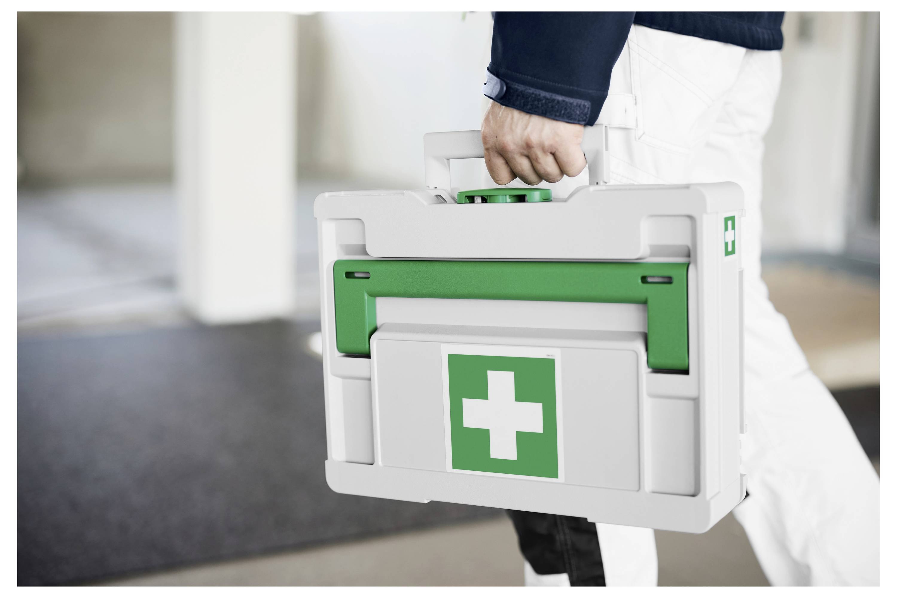 Person, die einen weißen Erste-Hilfe-Koffer mit grünem Kreuz trägt, was auf medizinische oder Notfallreaktion hinweist.