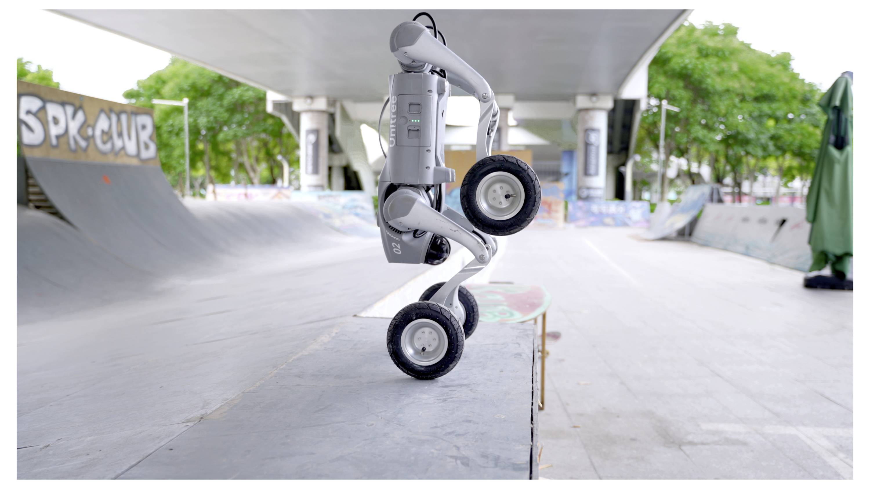 Vierrädriger Roboter, der aufrecht auf einer Skatepark-Kante unter einer Betonüberführung balanciert, mit Rampen und Graffiti im Hintergrund.