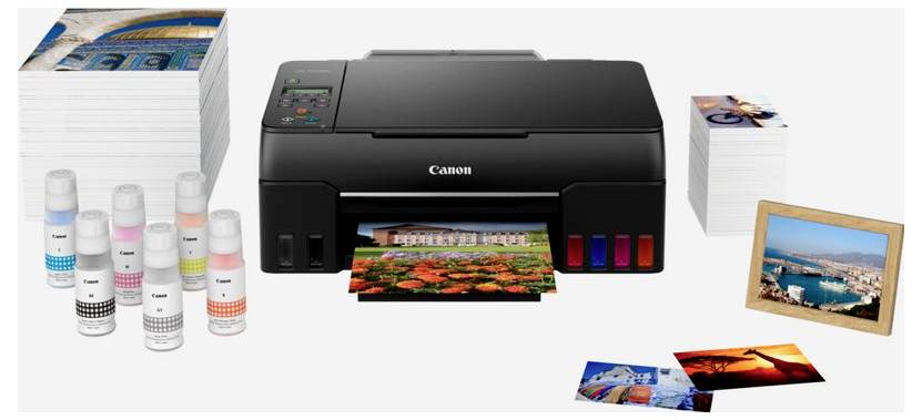 Canon-Drucker druckt ein farbenfrohes Foto, umgeben von Papierstapeln und Tintenflaschen, mit ausgedruckten Fotos in der Nähe.