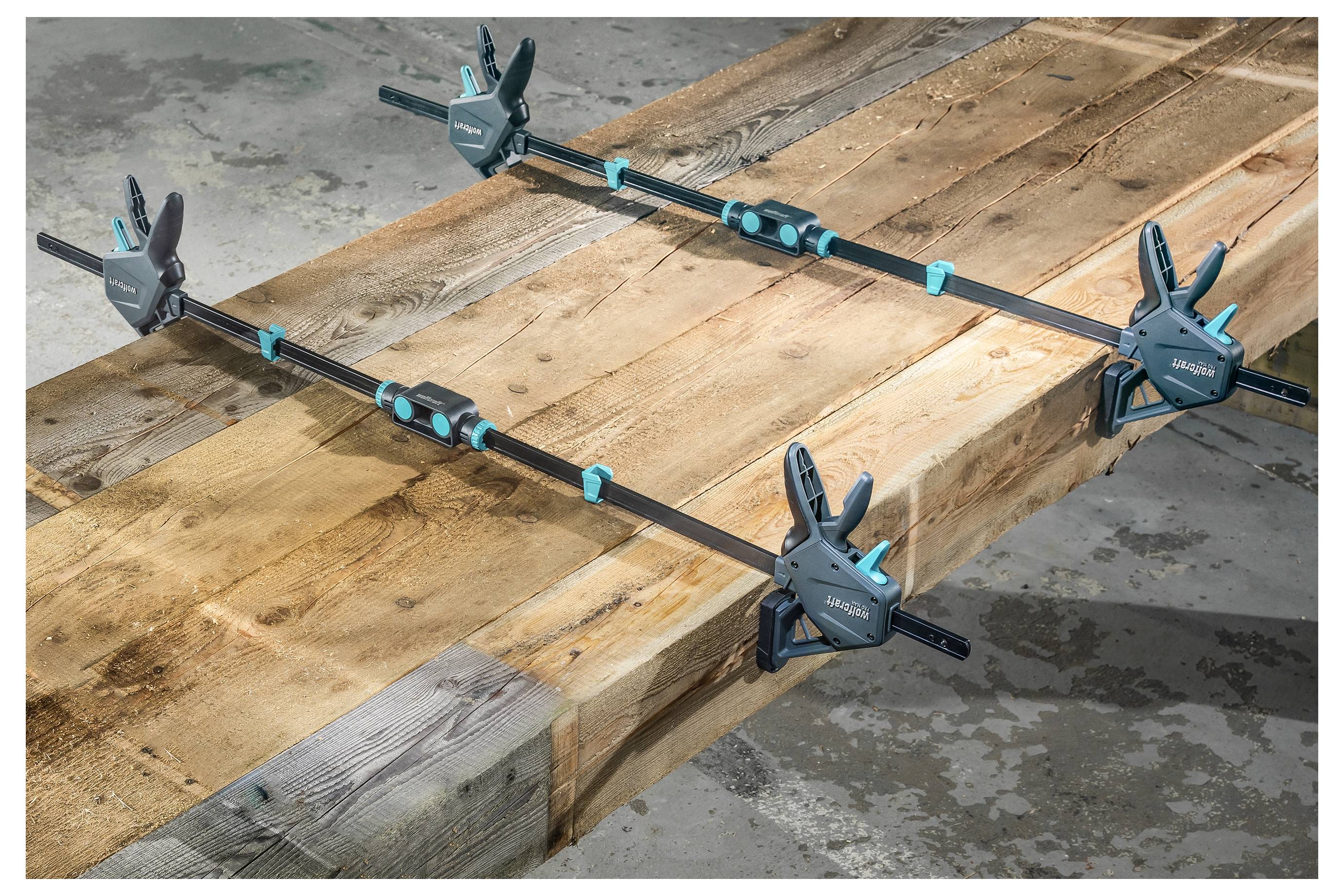 Holzbretter mit vier Schraubzwingen auf einer Werkbank zusammengespannt, wobei die Bretter zum Kleben oder Reparieren flach gehalten werden.