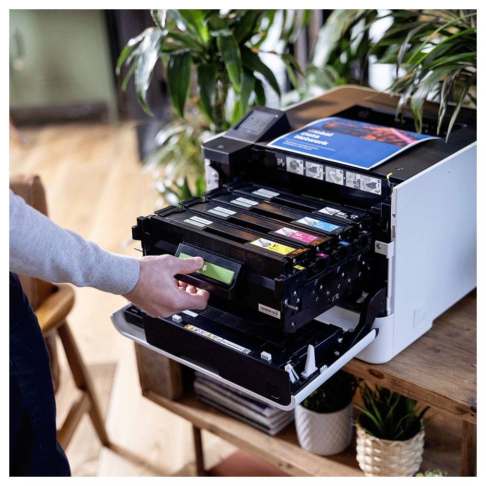 Eine Person setzt eine Tonerkartusche in einen offenen Laserdrucker auf einem Holztisch ein.