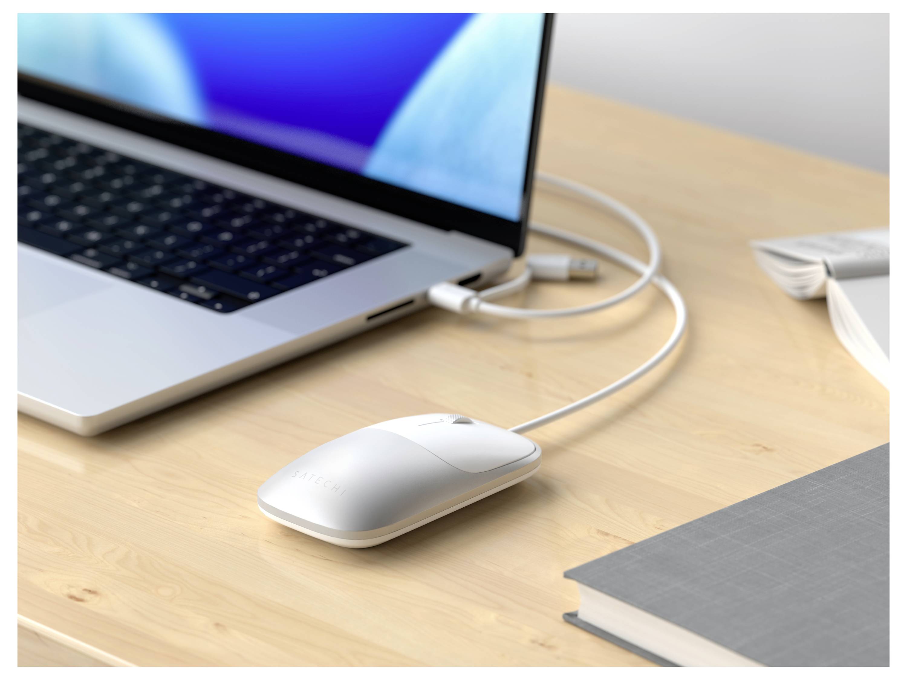 Laptop, der mit einer weißen Maus auf einem Holzschreibtisch verbunden ist, mit einem Buch und Papieren in der Nähe.