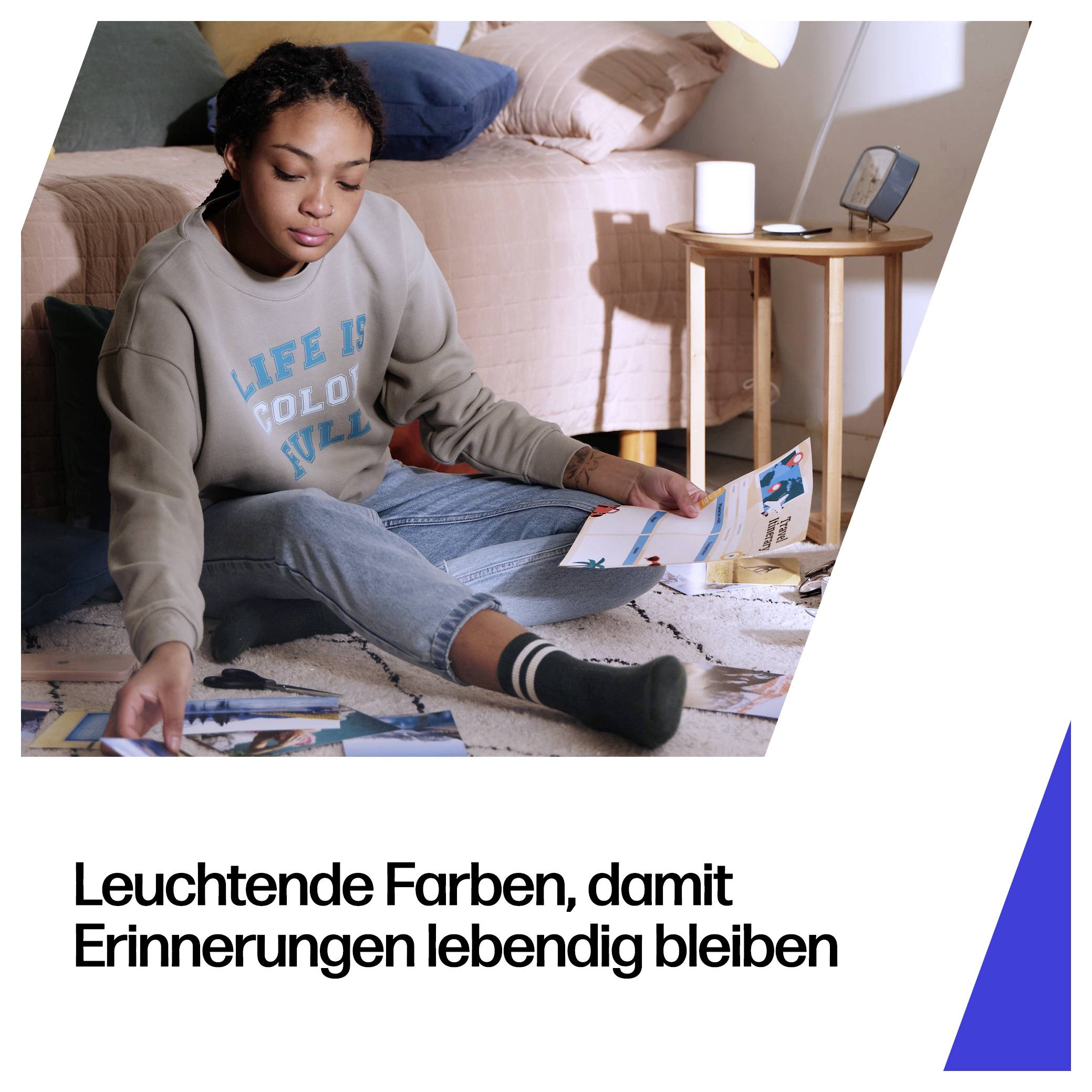 Junge Frau sitzt auf dem Boden und sortiert Fotoabzüge; deutscher Text lautet „Leuchtende Farben, damit Erinnerungen lebendig bleiben
