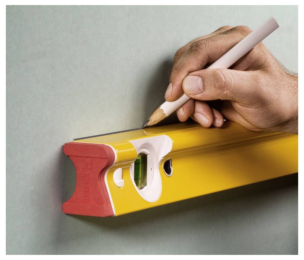 Hand hält einen Bleistift, um eine gelbe Wasserwaage zu markieren, was präzise Ausrichtung oder das Zeichnen einer geraden Linie anzeigt.