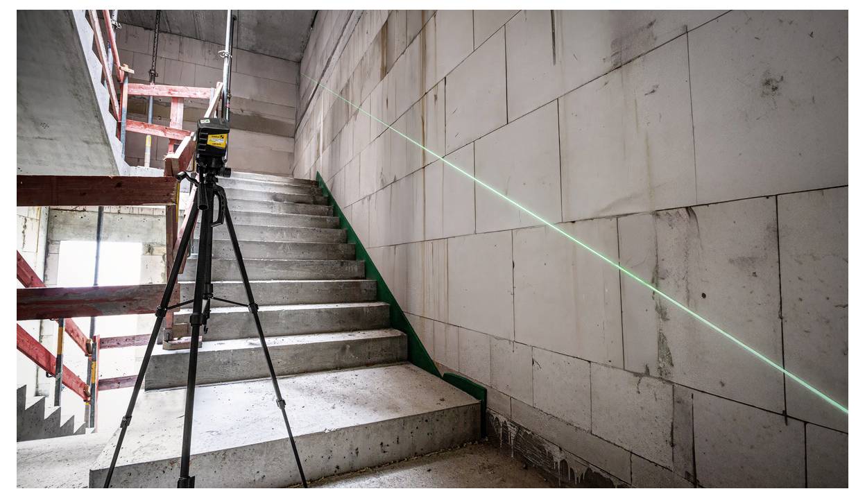 Laserpegel auf Stativ projiziert eine grüne Linie entlang einer unvollendeten Betontreppe auf einer Baustelle.