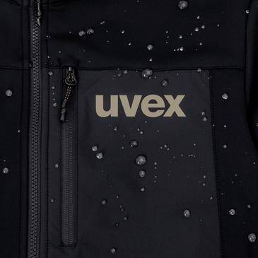 Nahaufnahme einer schwarzen uvex-Jacke mit Wassertropfen, die auf dem Stoff perlen, und einer vorderen Reißverschlusstasche, die die Wasserfestigkeit zeigt.
