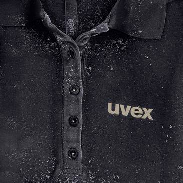 Nahaufnahme eines schwarzen uvex Poloshirts mit sichtbarem Markenlogo, bedeckt mit Staub oder Pulver.