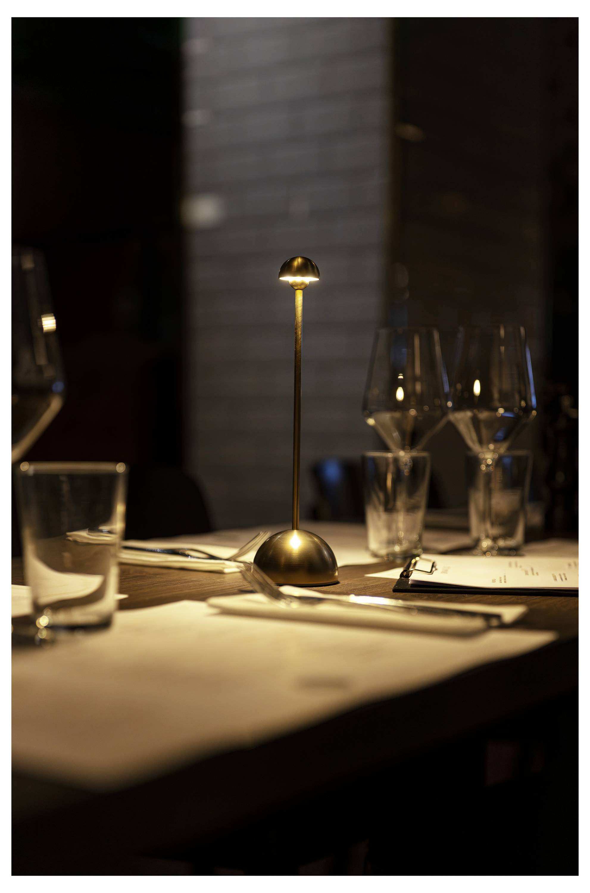 Tisch im Kerzenschein in einem Restaurant mit Gläsern, Besteck, Speisekarten und einer kleinen Lampe, die eine elegante Dinneratmosphäre schafft.