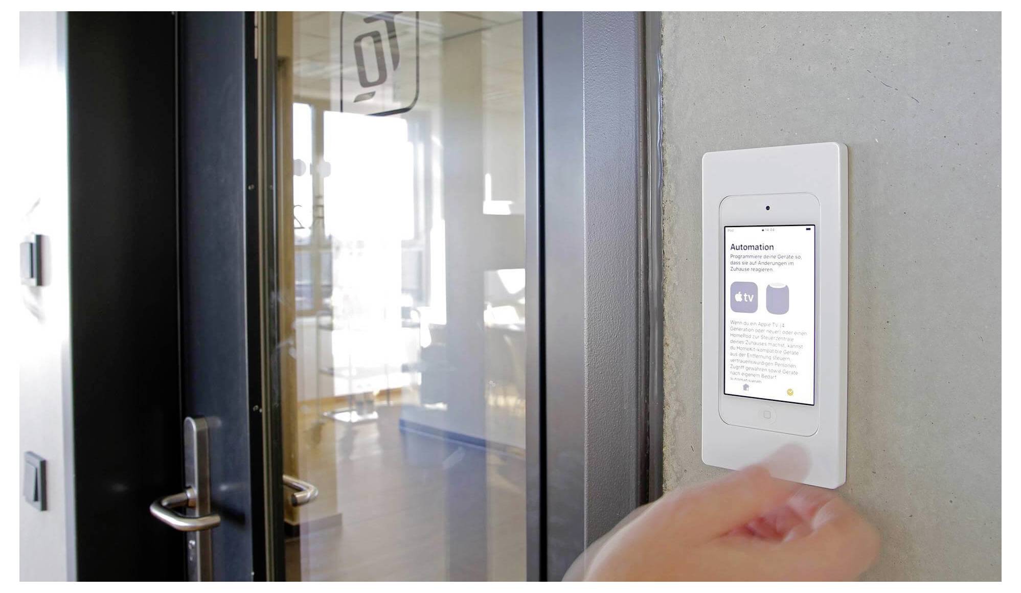 Hand drückt ein wandmontiertes Smart-Zugangspanel neben einer gläsernen Bürotür, um den Zutritt freizugeben oder zu kontrollieren.