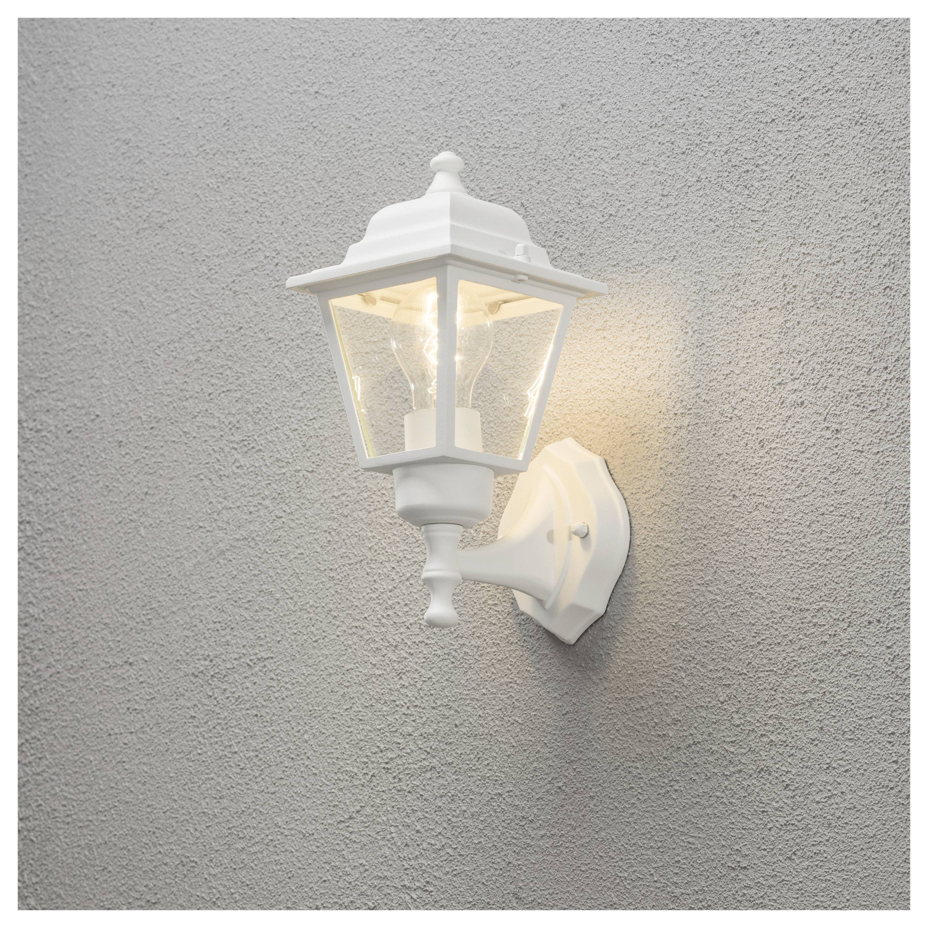 Weiße Außenwandleuchte auf einer strukturierten grauen Stuckwand montiert, beleuchtet und warm leuchtend.