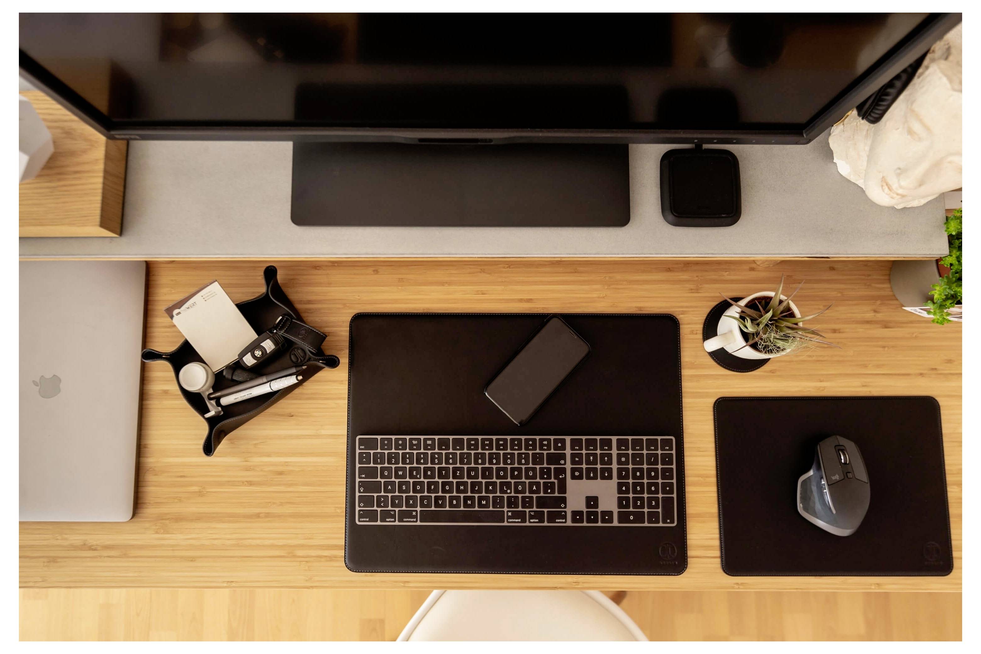 Draufsicht auf einen aufgeräumten Schreibtisch mit einem Laptop, einer Maus, einem Monitor, einem Telefon, Kopfhörern und einer kleinen Pflanze, die ein Arbeits- oder Home-Office-Setup suggeriert.