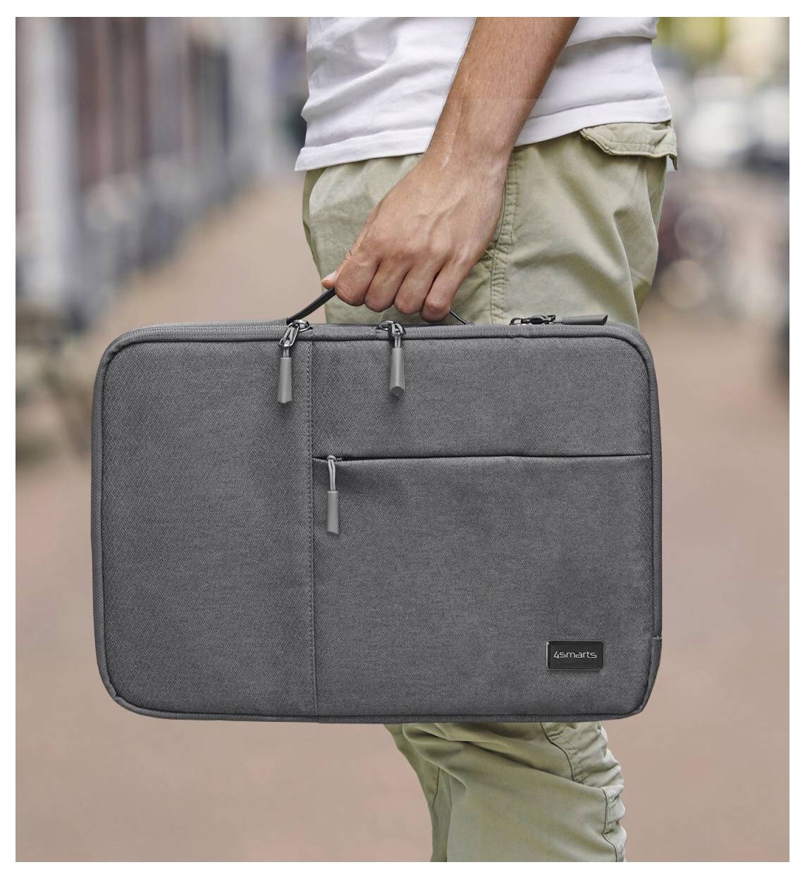 Nahaufnahme einer Person, die draußen eine graue Laptoptasche mit Reißverschluss am Griff hält.