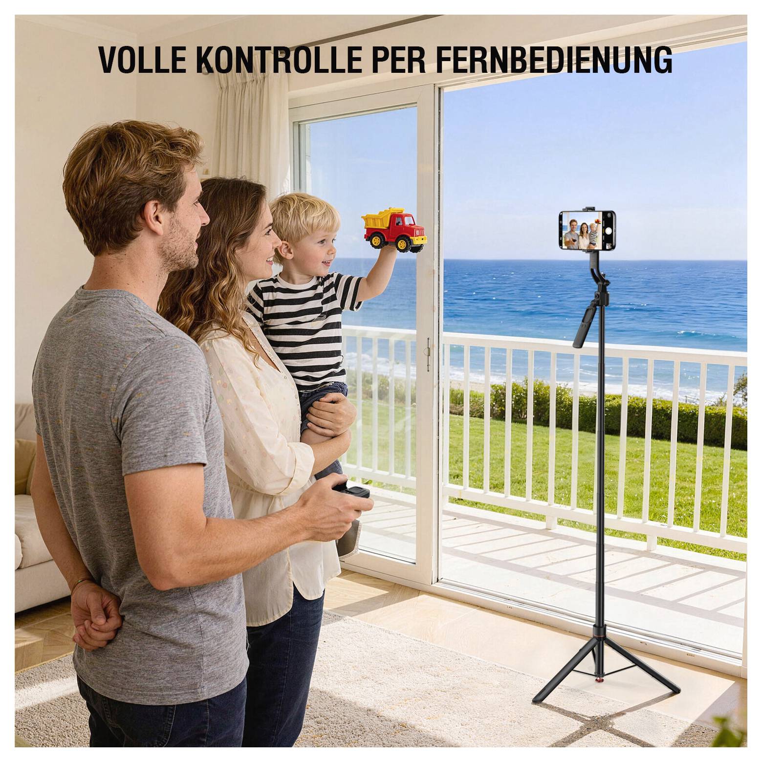 Familie in einem Zimmer am Meer kontrolliert ein Smartphone auf einem Stativ mit einer Fernbedienung; Text lautet „VOLLE KONTROLLE PER FERNBEDIENUNG".