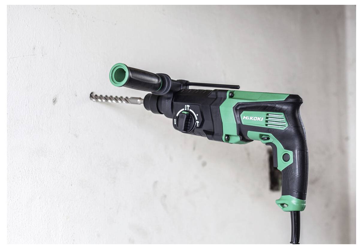 Ein schwarz-grüner schnurgebundener elektrischer Bohrer mit einem Mauerwerksbohrer ist an einer weißen Wand montiert und bereit zum Bohren.