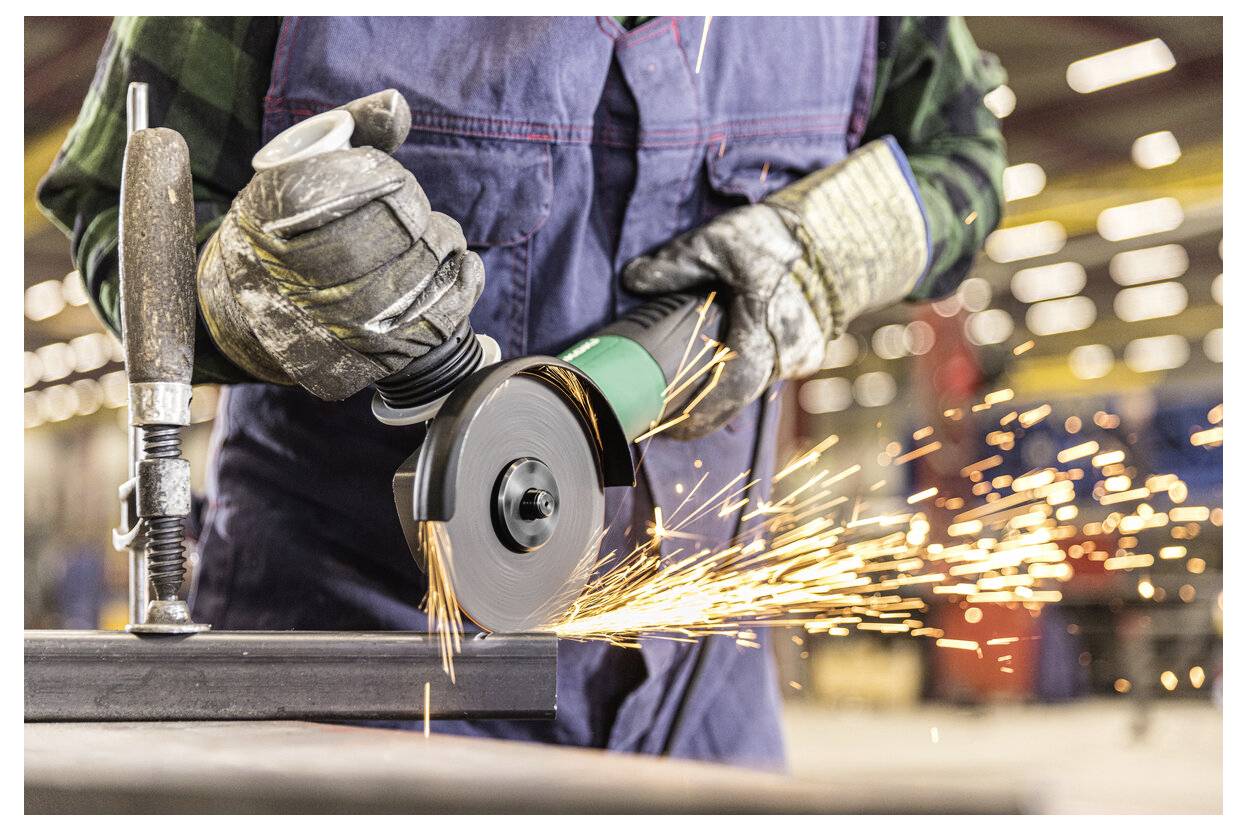 Ein Arbeiter benutzt einen Winkelschleiffer auf Metall und erzeugt dabei leuchtend helle Funken, die über den Werkstattboden sprühen.