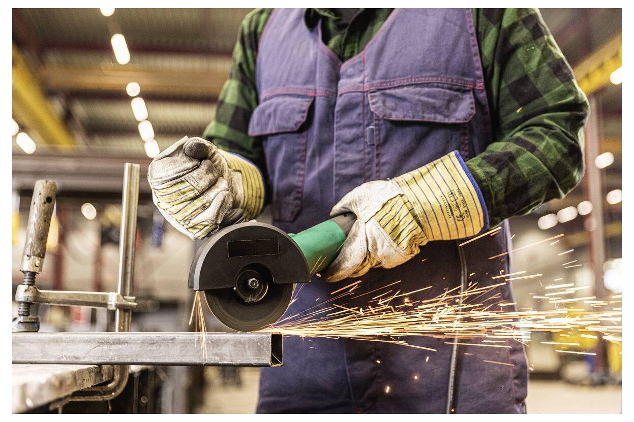 Arbeiter mit Handschuhen, der einen Winkelschleifer auf Metall einsetzt und Funken in der gesamten Werkstatt versendet.