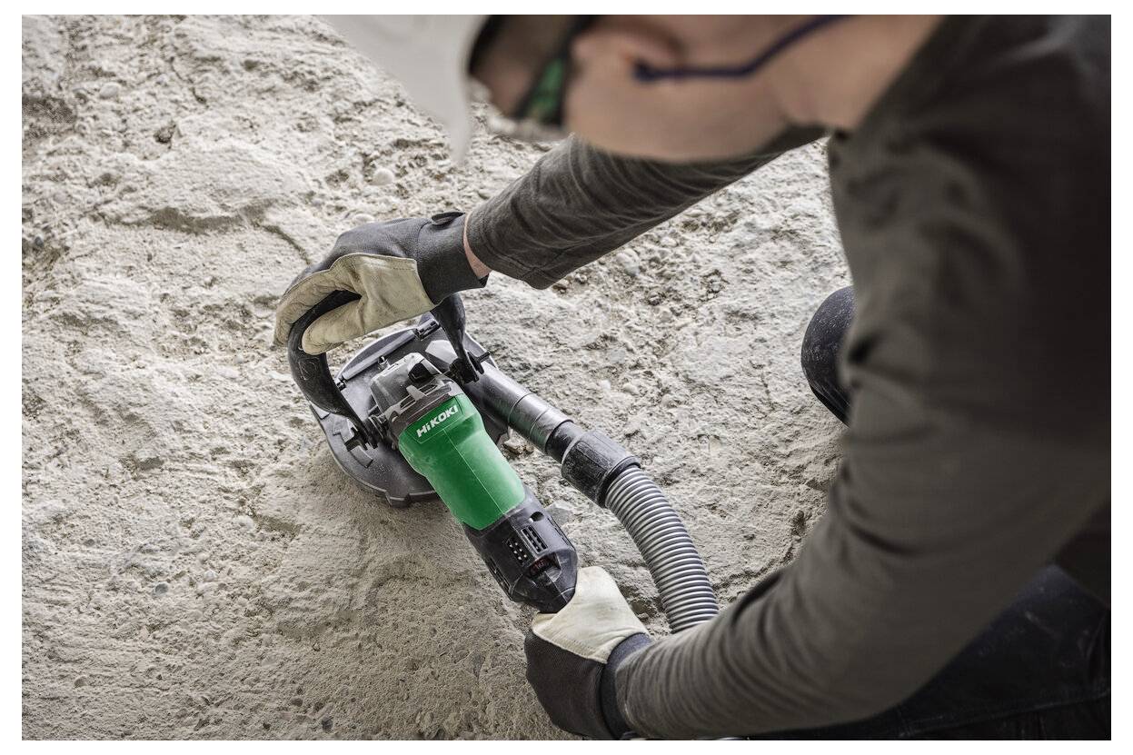 Arbeiter, der mit einem tragbaren Elektroschleiffer eine Nut in eine Steinmauer schneidet, mit angeschlossener Staubabsaugschlauch.