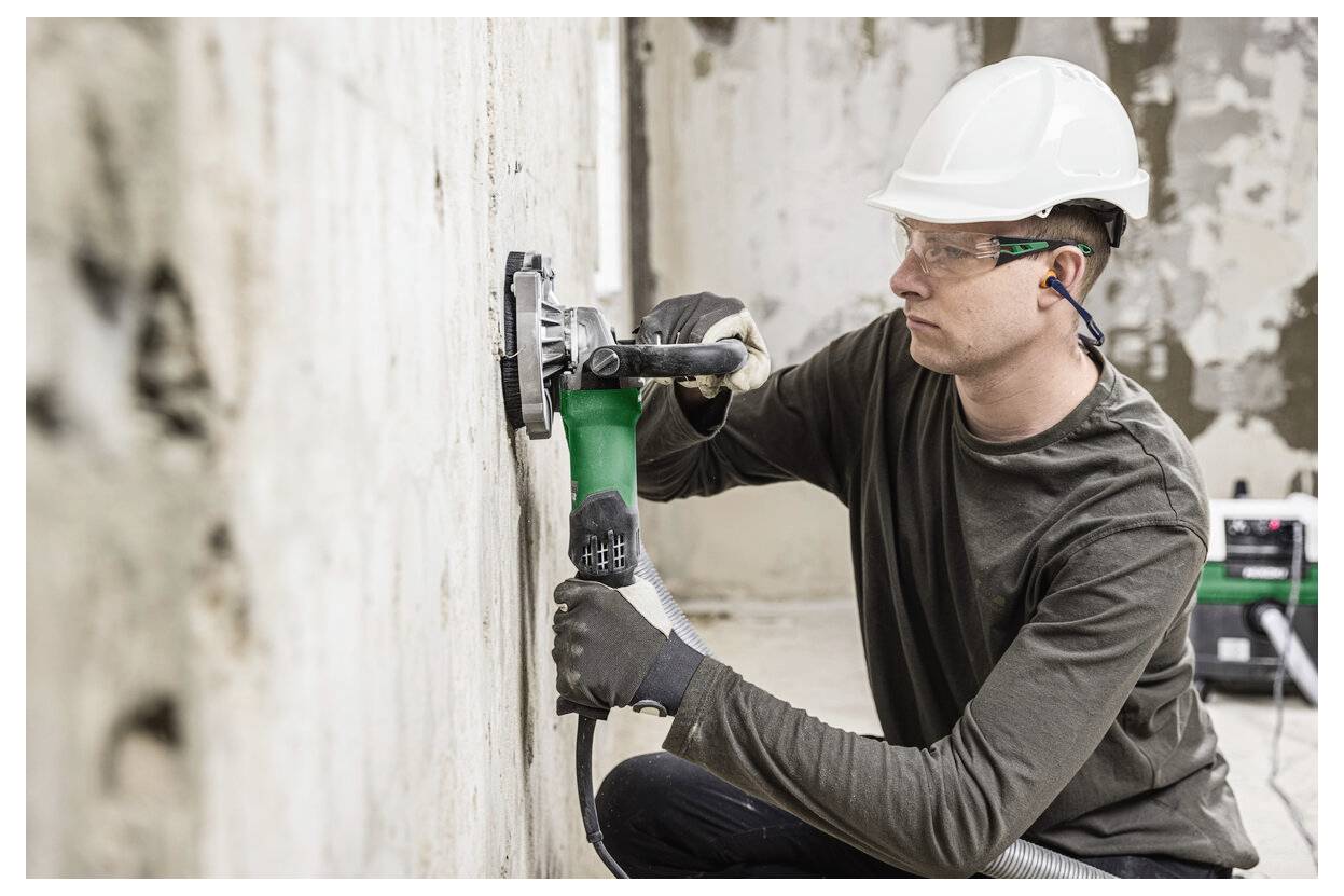 Ein Bauarbeiter in einem Schutzhelm benutzt einen Elektroschleiffer an einer Wand während einer Renovierung im Innenbereich.