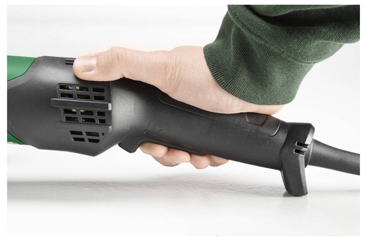 Nahaufnahme einer Hand, die ein grün-schwarzes Elektrowerkzeug an seinem Griff hält, mit dem angeschlossenen Kabel, auf weißem Hintergrund.