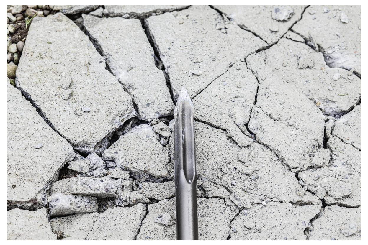 Ein Metallmeißel zeigt auf gerissenen, beschädigten Beton und deutet auf Oberflächenschäden oder Abbrucharbeiten hin.
