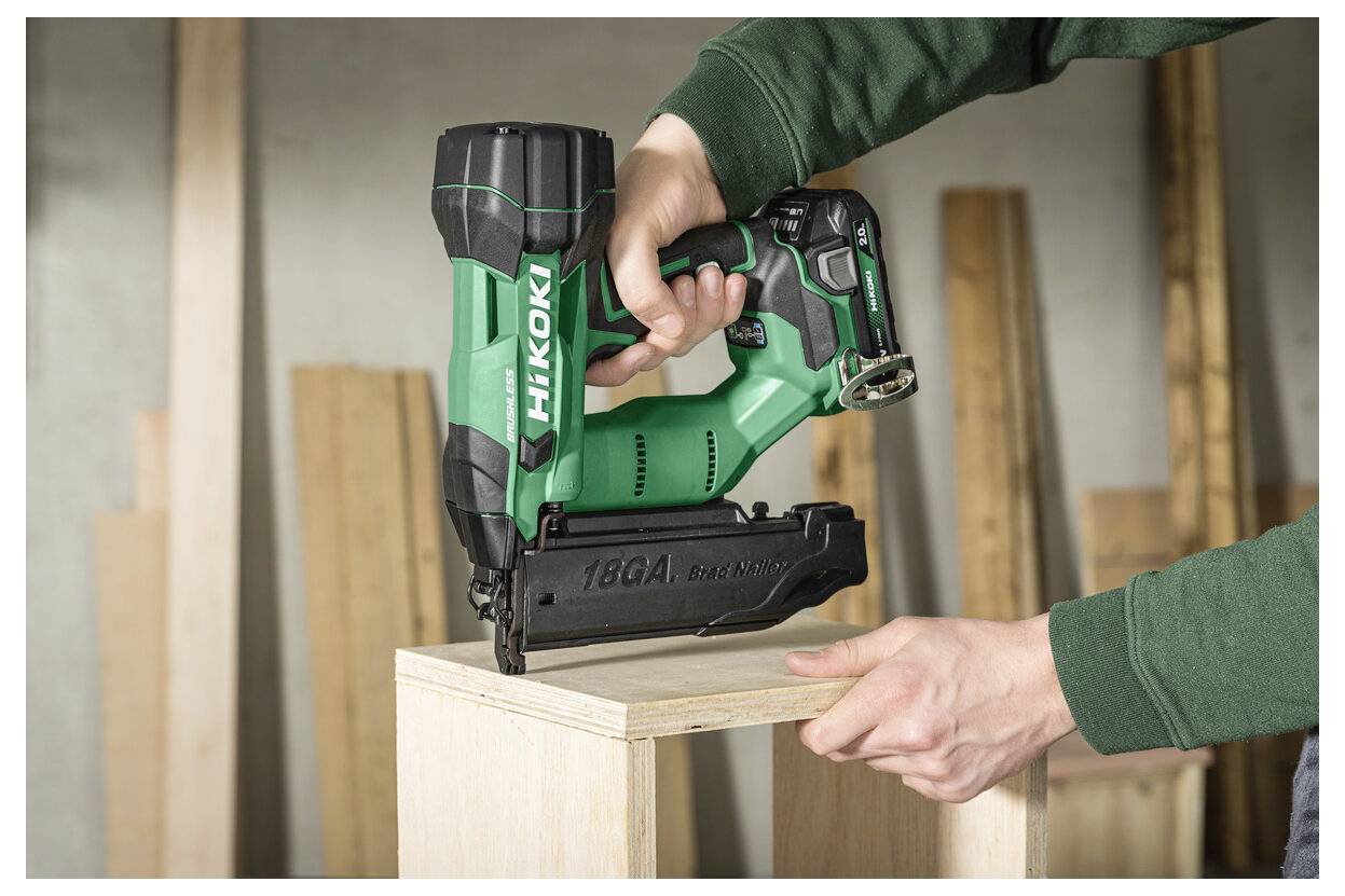 Eine Person verwendet einen grünen kabellosen Nagler, um einen Holzkistenrahmen in einer Werkstatt zu befestigen.